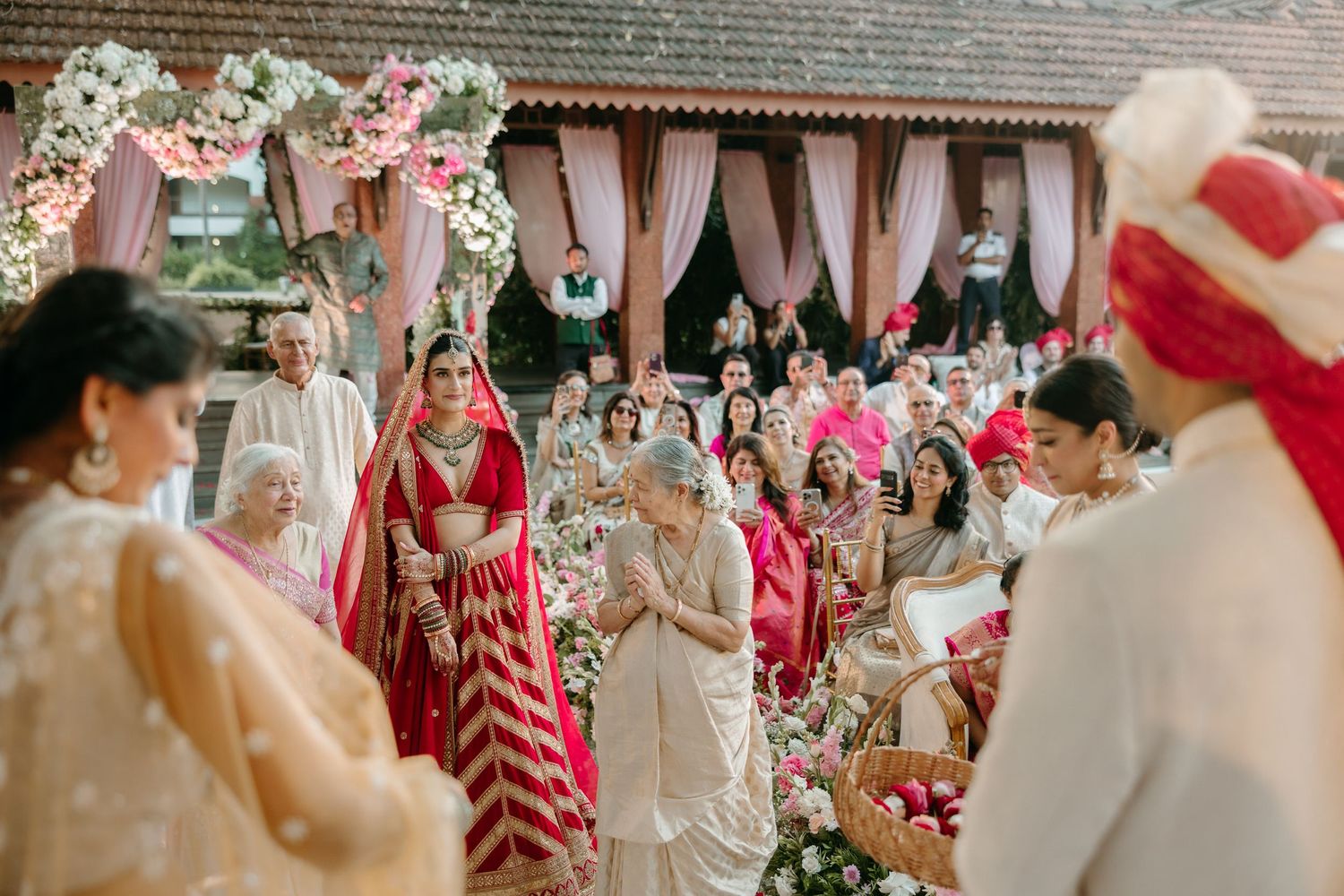 Wedding ceremony decorations feature pink and red floral arrangements with elegant white drapery in an outdoor setting.