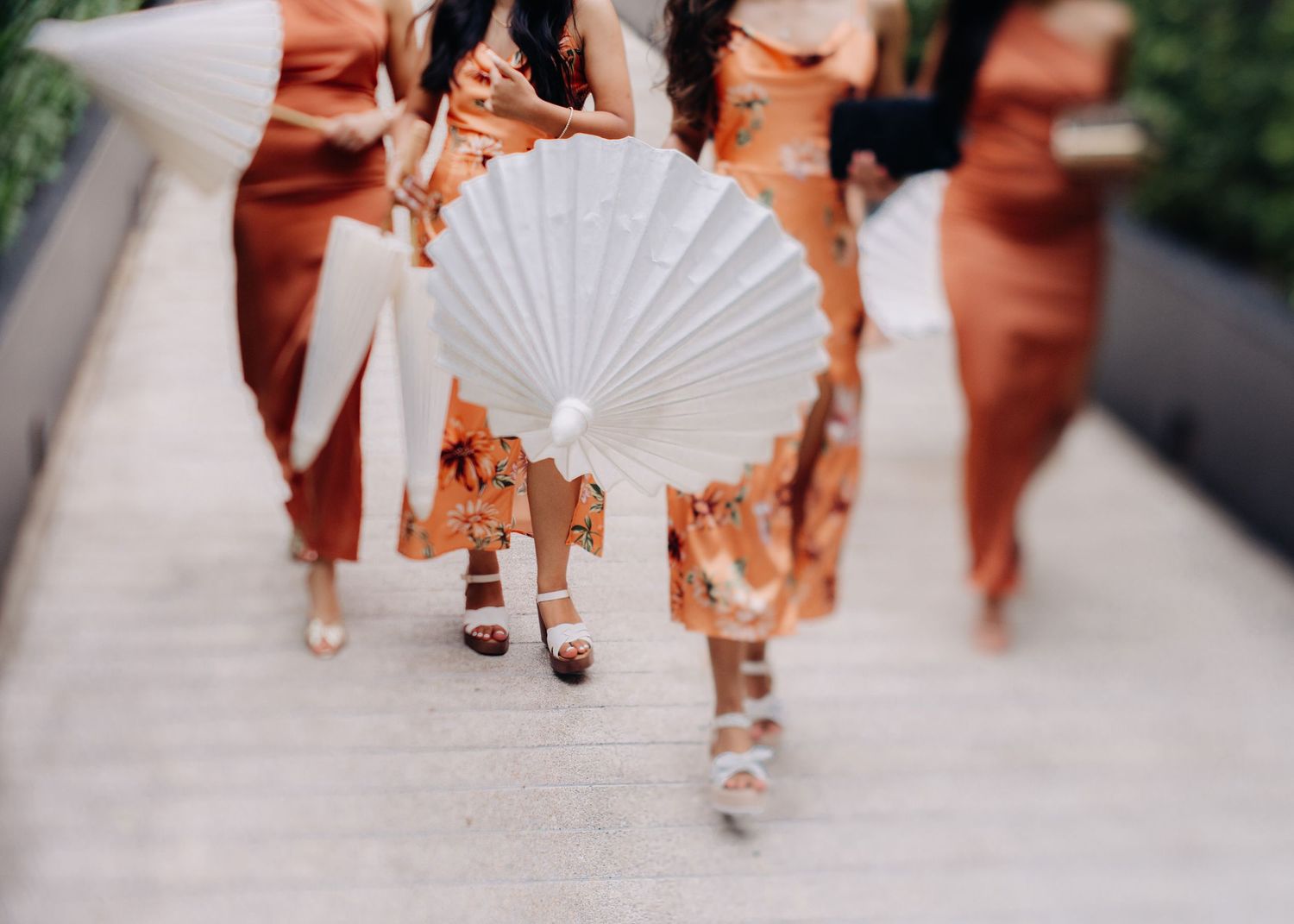 A white paper fan held by someone wearing a peach-colored dress walking alongside others in matching attire.