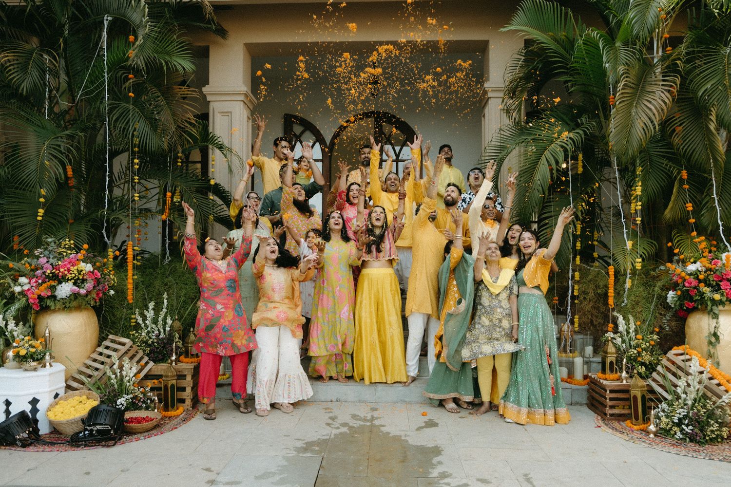 Wedding party stands together in tropical garden setting with yellow dresses and floral decorations.