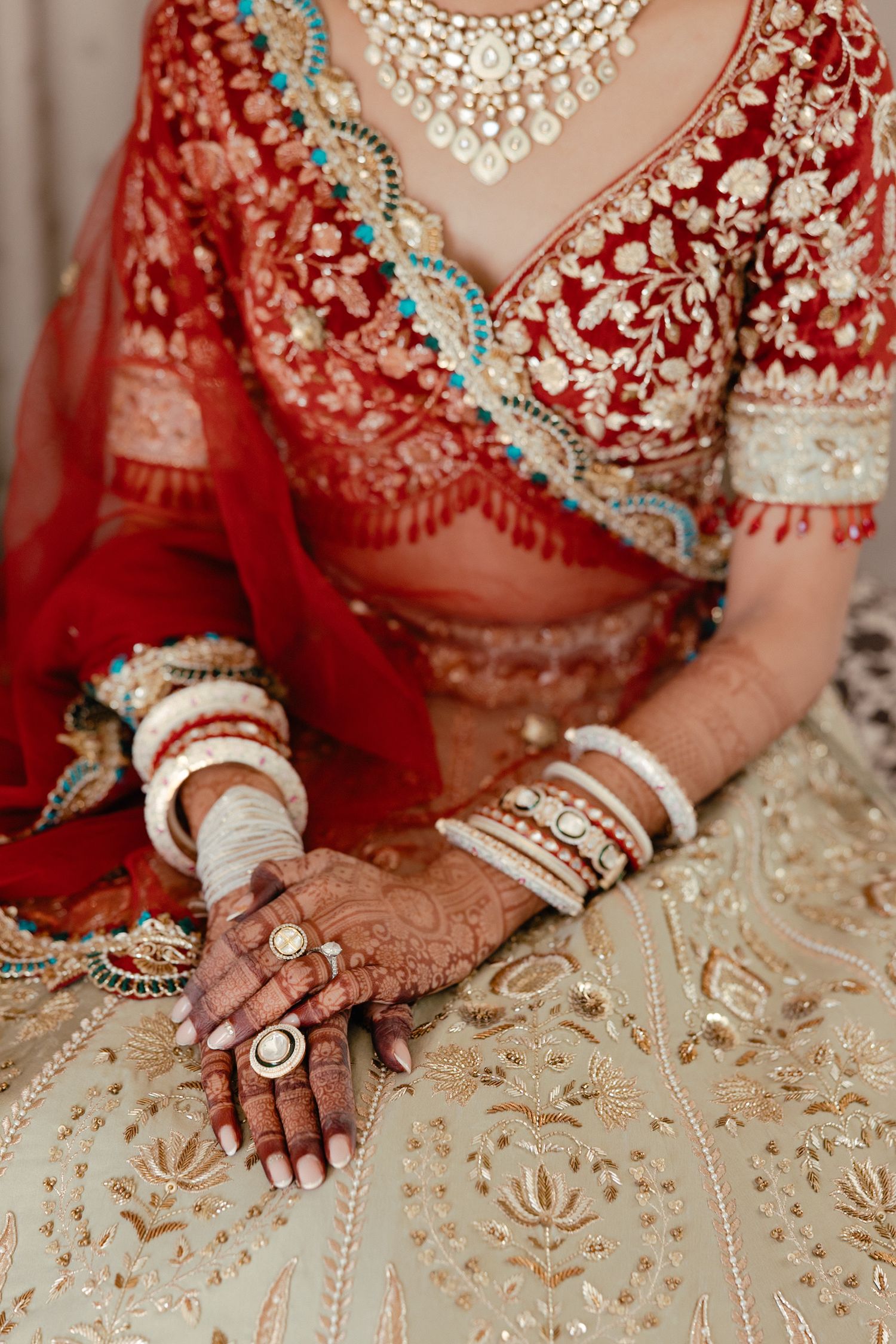 Close-up details of traditional Indian bridal jewelry and henna adorned hands against gold embroidered fabric.