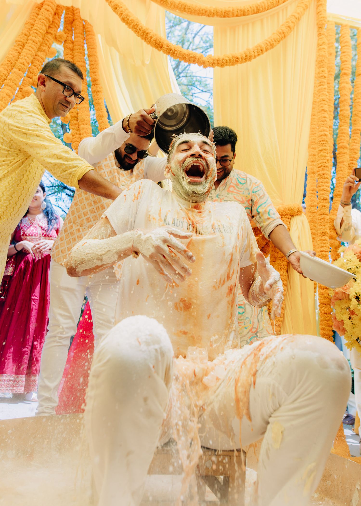 Joyful celebration during a Haldi ceremony with yellow turmeric powder being poured during traditional Indian pre-wedding ritual.