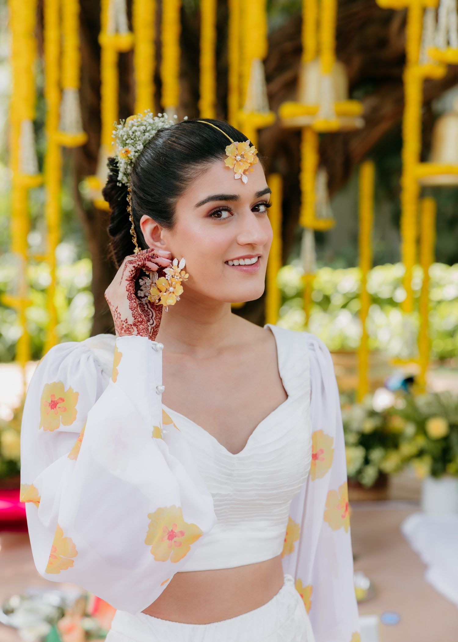 A bride in a white outfit with traditional Indian wedding decor featuring marigold garlands in the background.