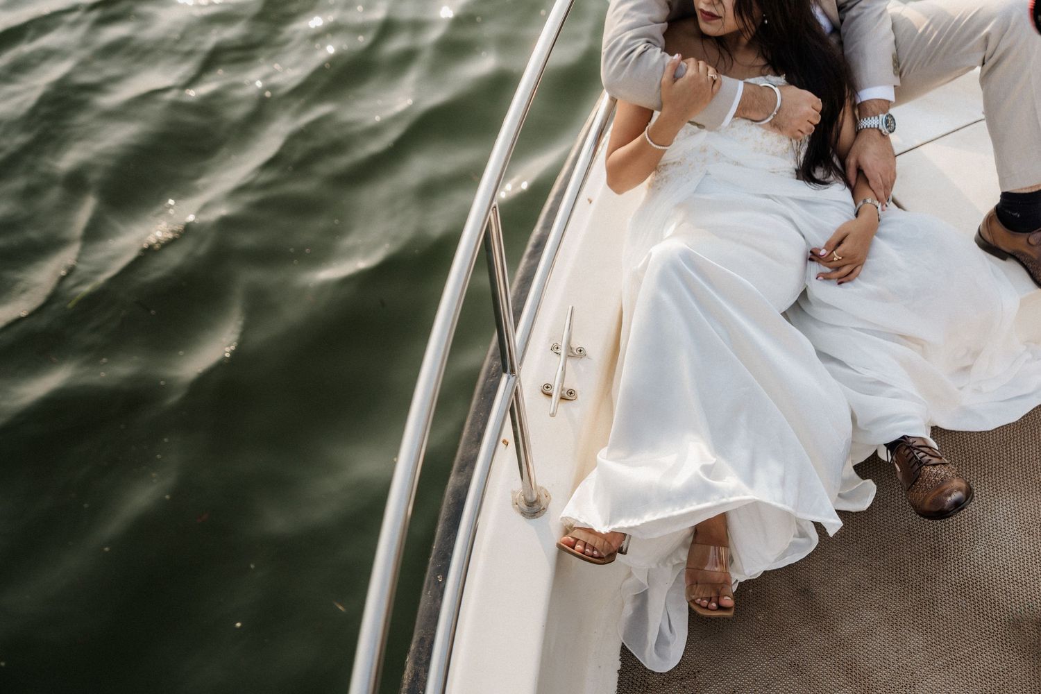 A couple in white outfits poses together on a boat deck during their romantic seaside wedding ceremony.