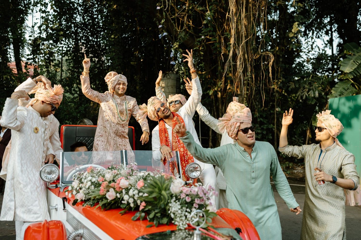 Wedding party celebrates outdoors with joyful dancing and laughter in a garden setting.