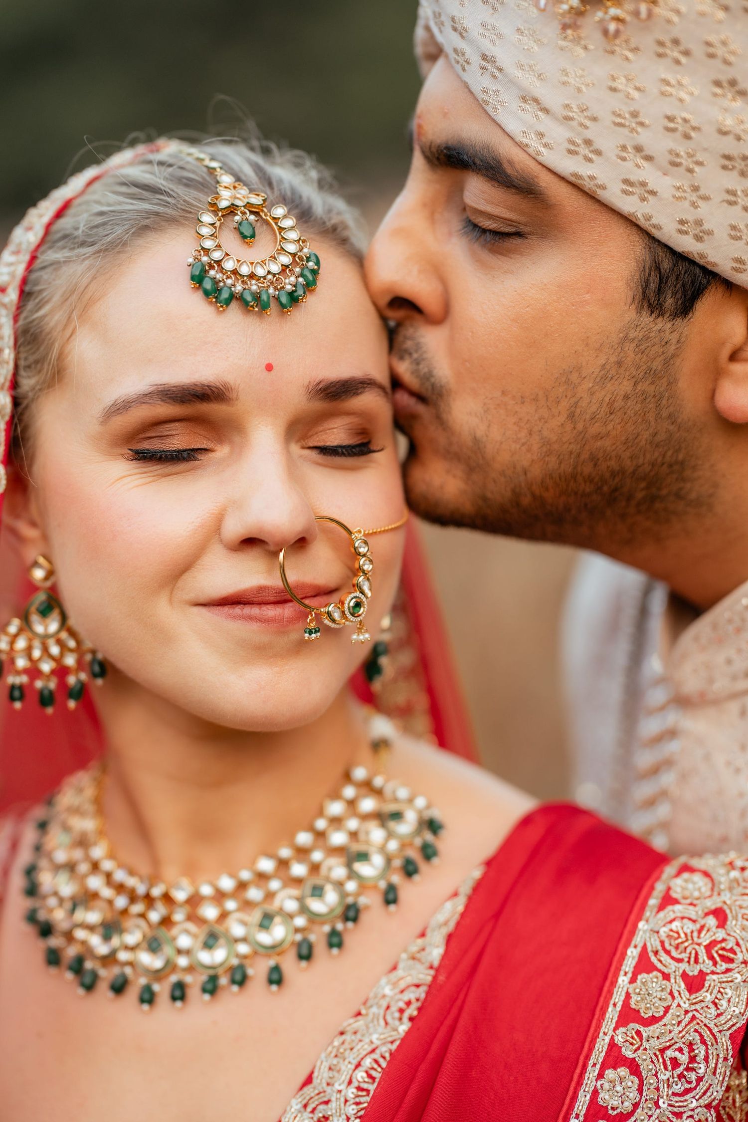 Close-up of wedding couple wearing traditional Indian jewelry and attire sharing intimate moment.
