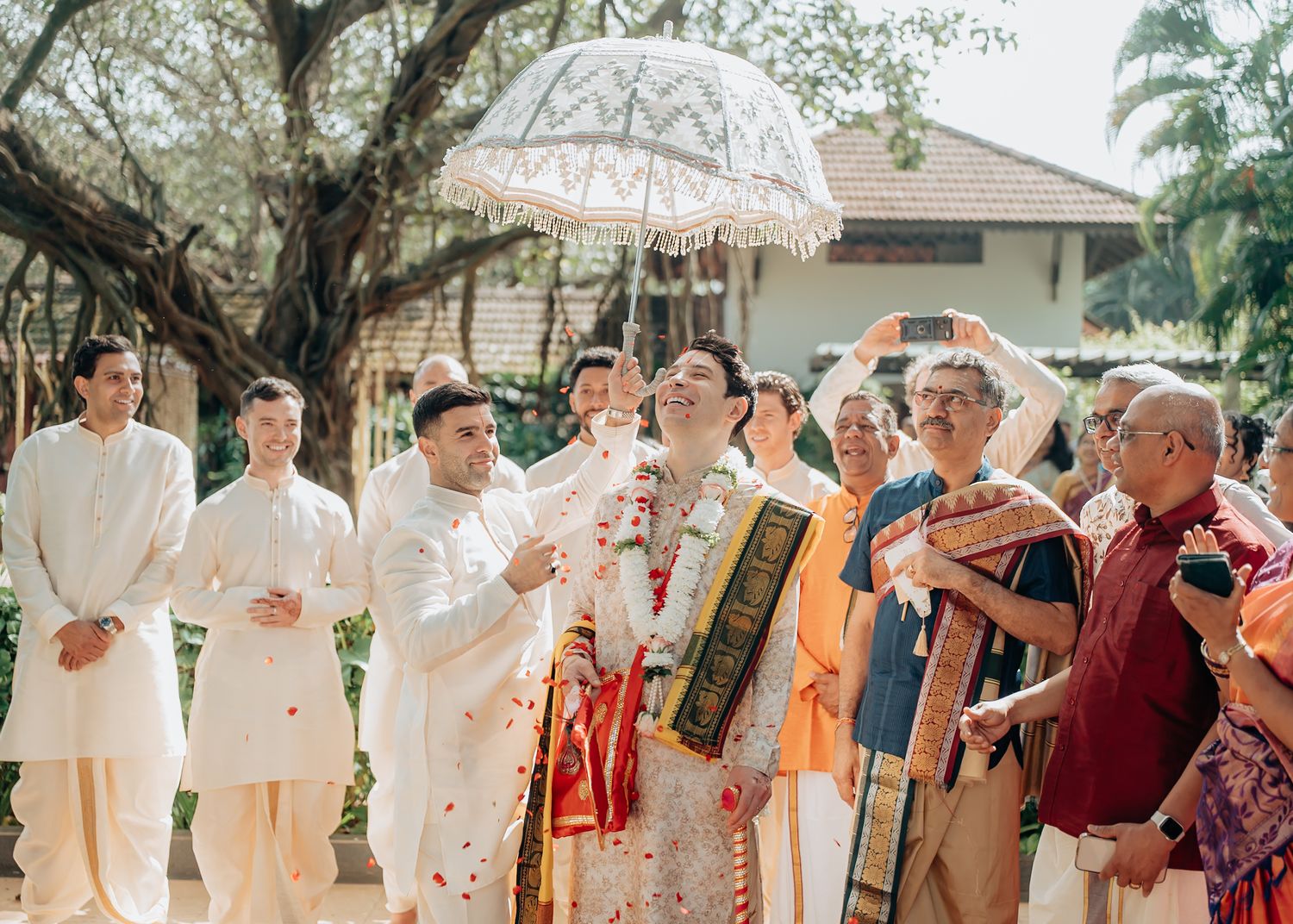 Wedding party and guests gathered outdoors under trees for group photos.