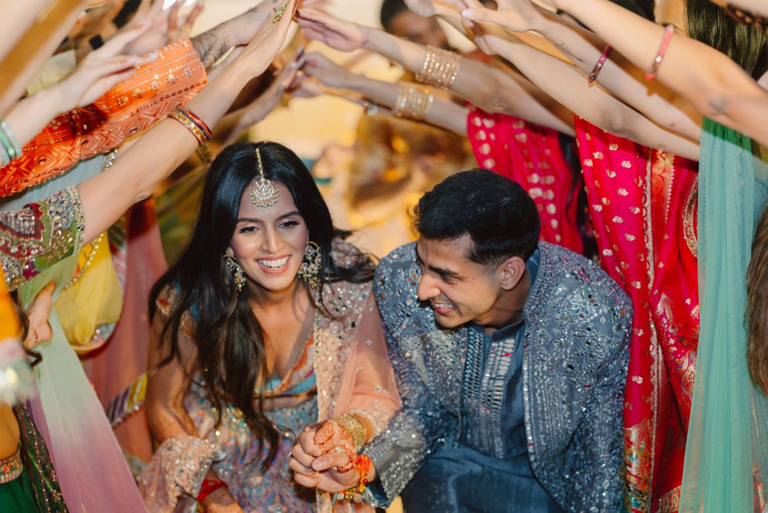 A couple shares a joyful moment under colorful fabric decorations at their Indian wedding celebration.