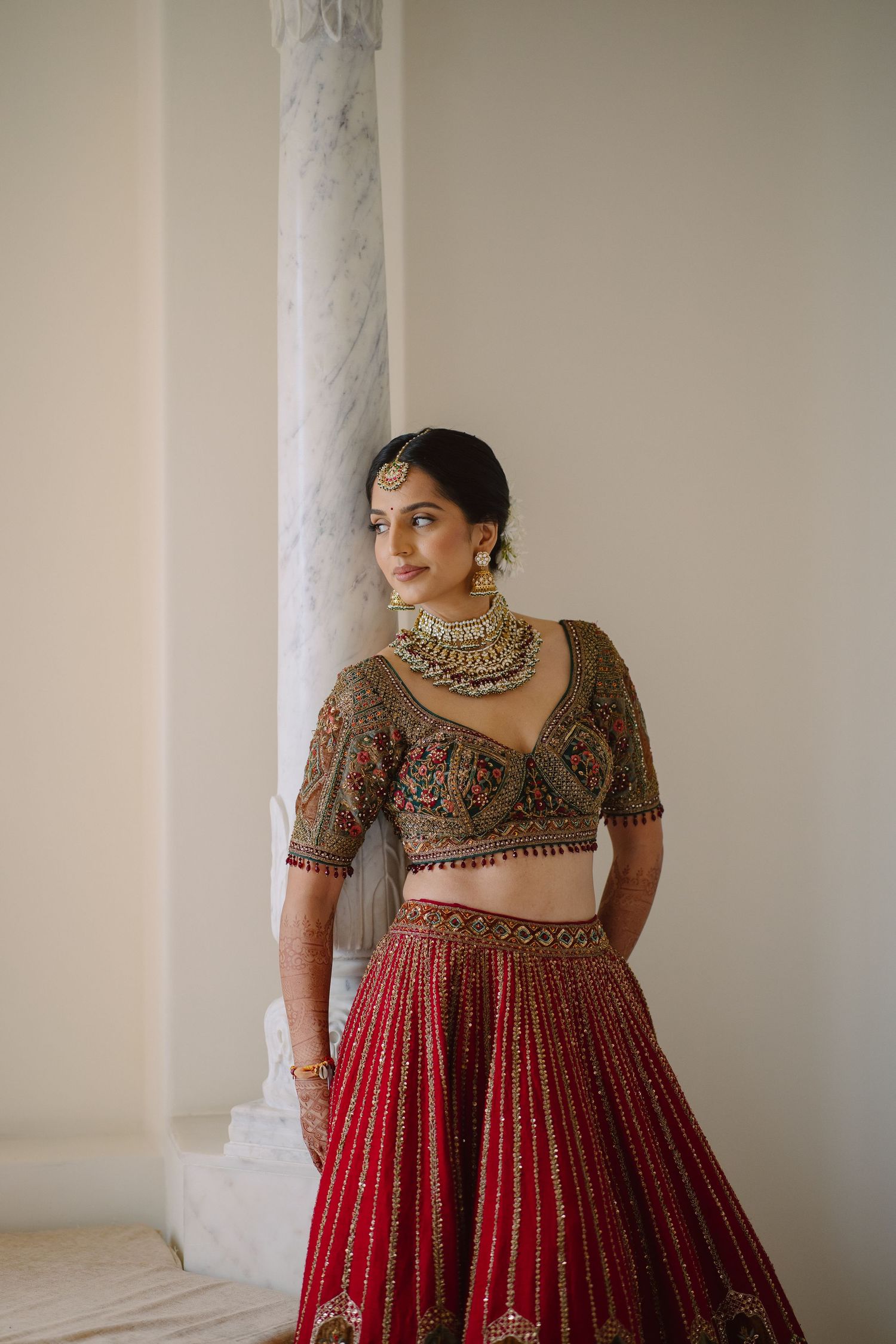 Traditional Indian bridal outfit featuring red pleated lehenga and embroidered blouse with statement jewelry.