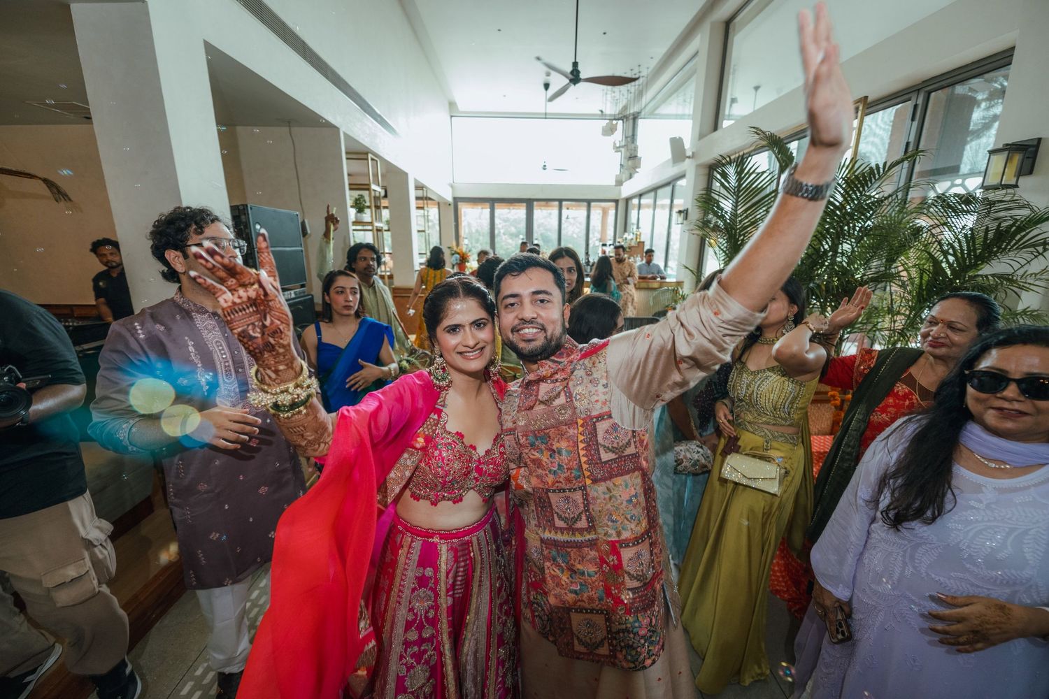 Joyful Indian couple in traditional wedding attire celebrating with guests at a vibrant indoor wedding ceremony.