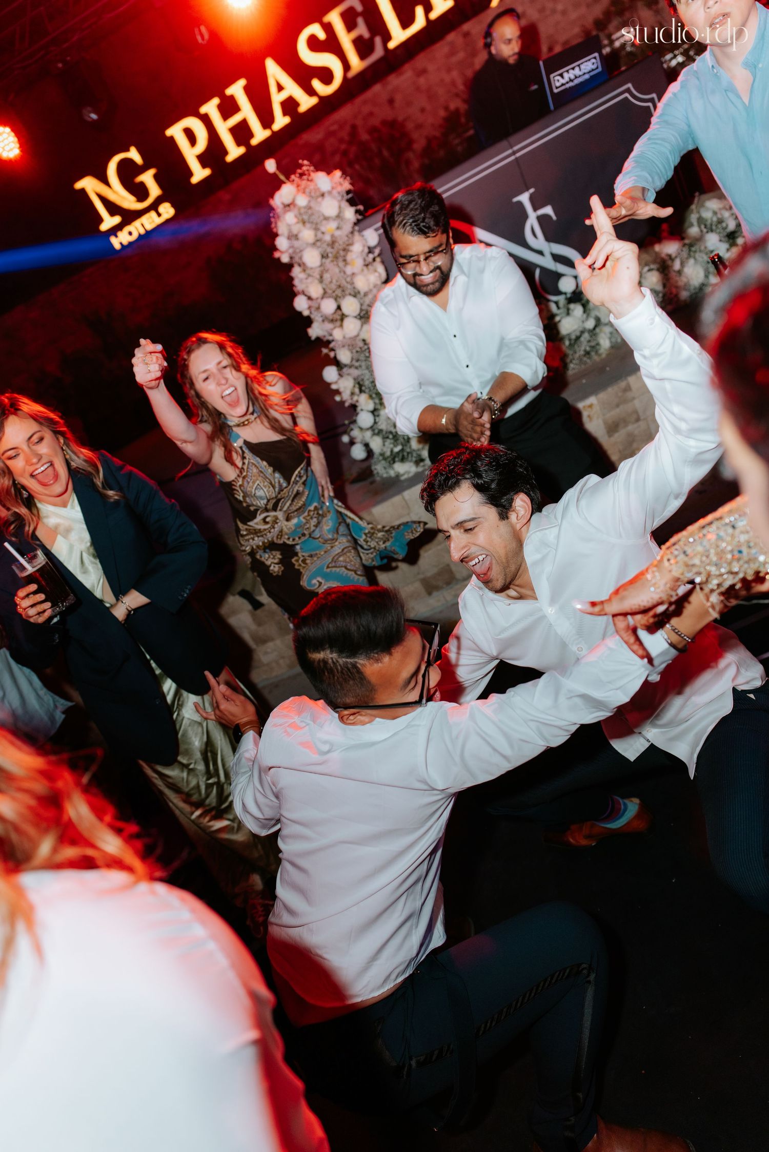 Guests dancing energetically at NG Phaseli Hotels party event, men in white shirts celebrating on the dance floor.