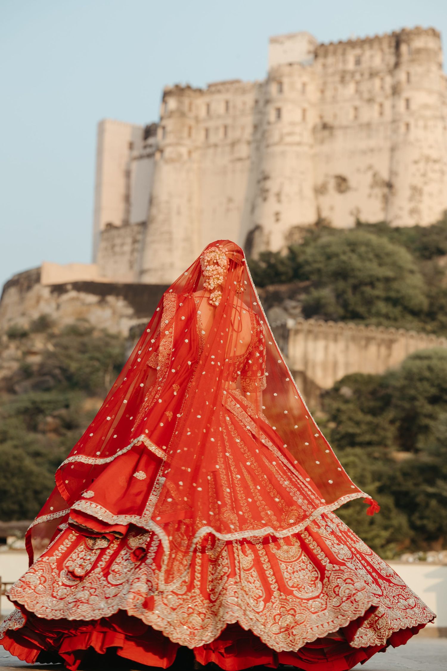 Red and gold lehenga dress spinning in multiple frames with ancient fort in background.