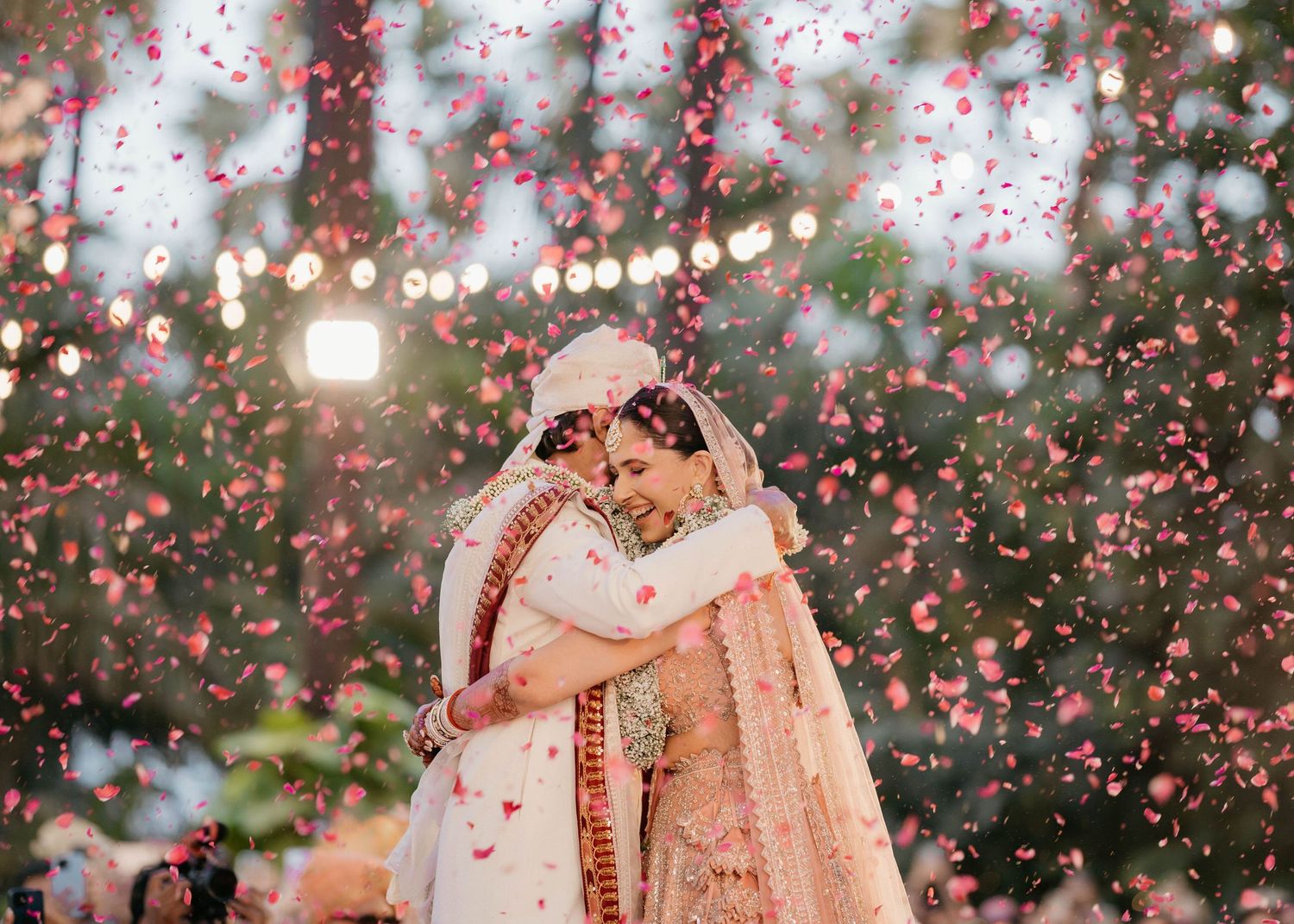 Pink flower petals fall amidst twinkling lights during a traditional Indian wedding celebration.