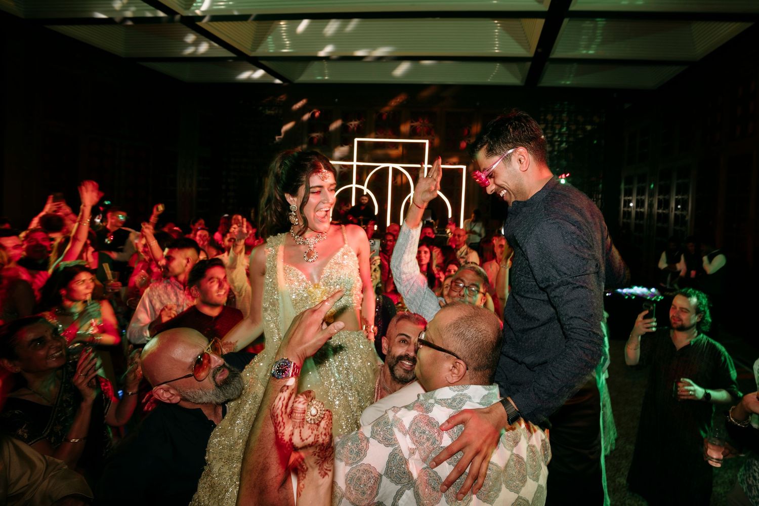 Party guests dance and mingle at a nightclub with red lighting and a dark ambiance during a celebration.