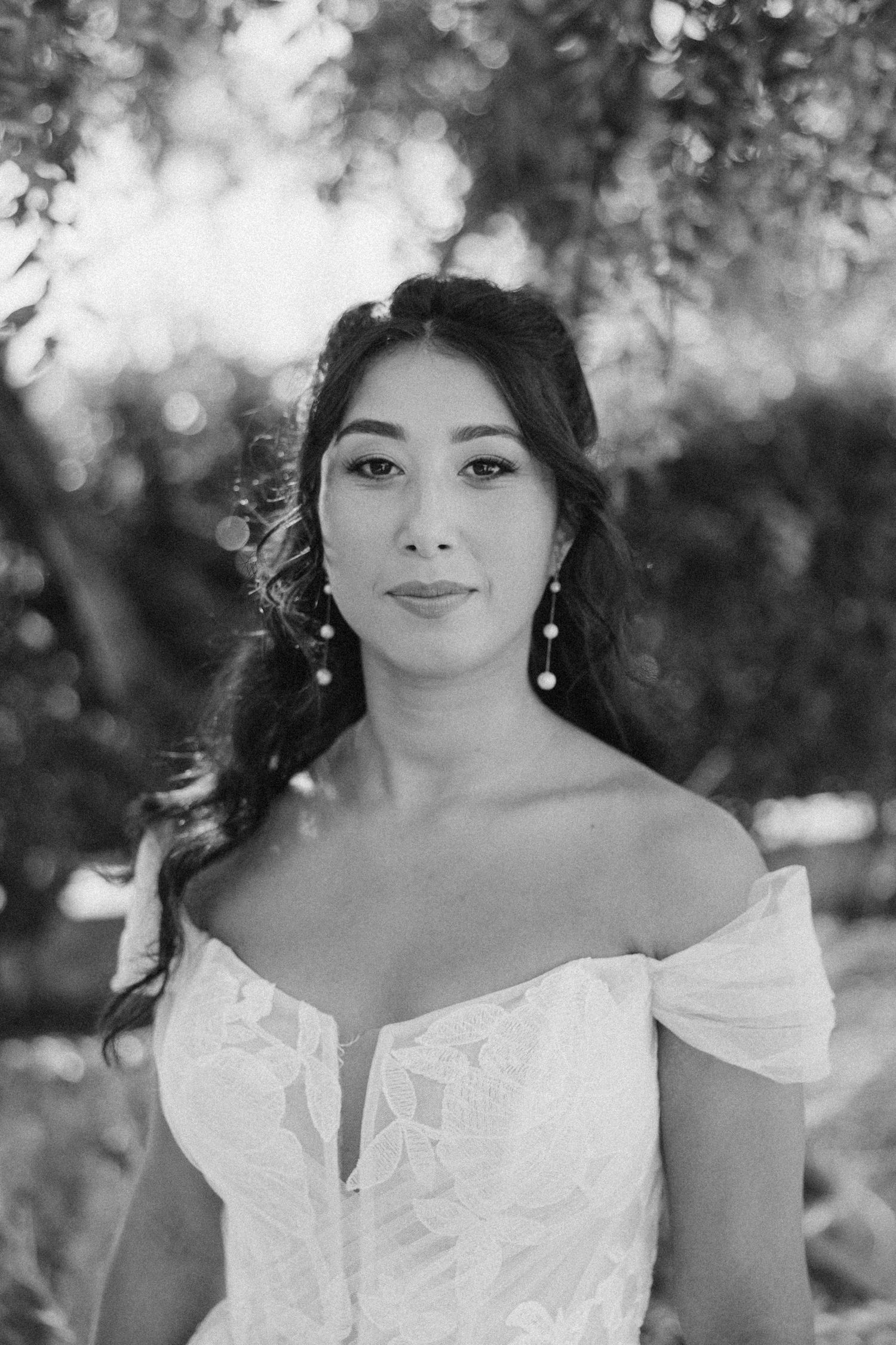 Close-up black and white portrait of a bride wearing an off-shoulder wedding gown and delicate earrings.