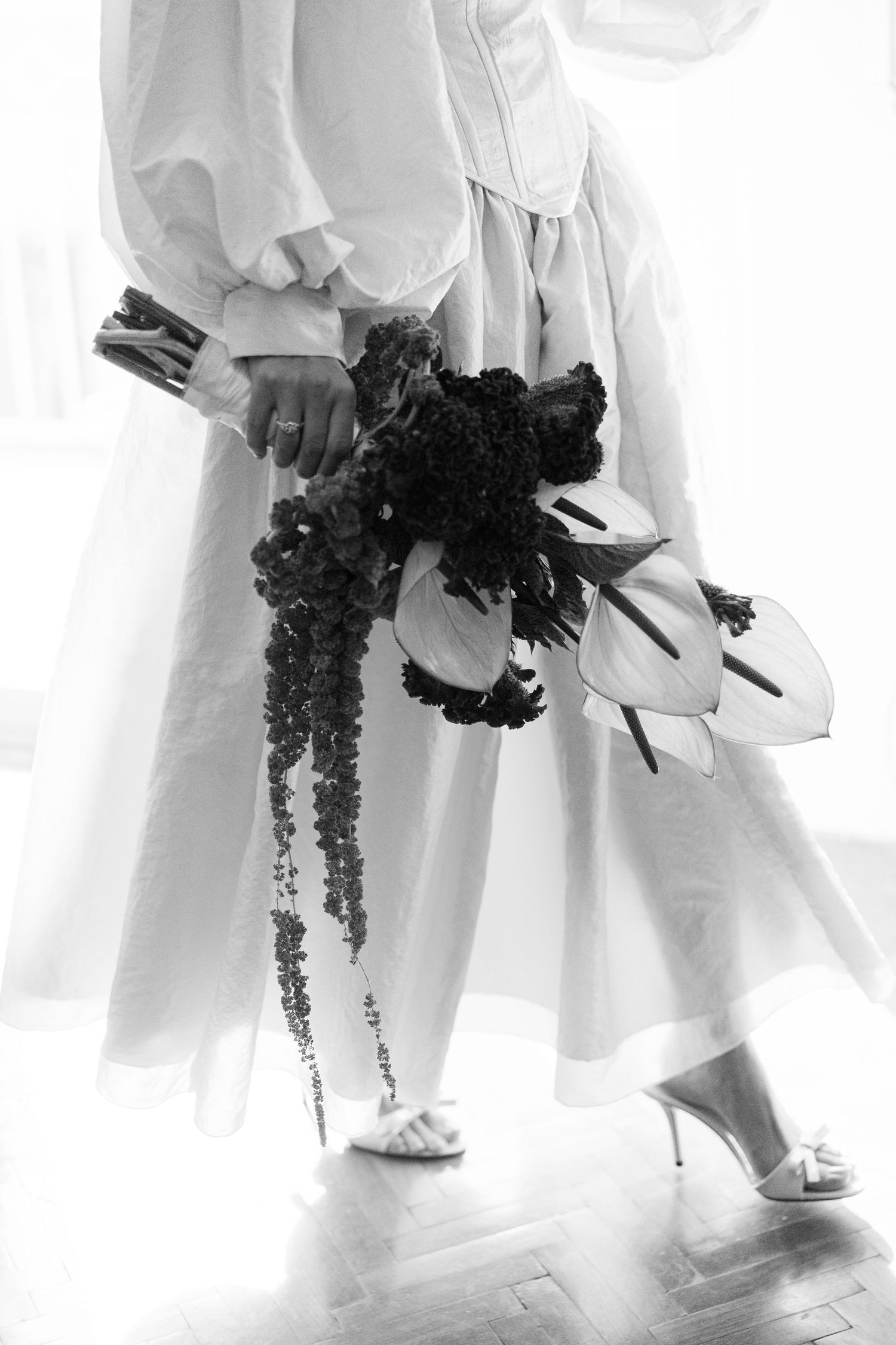 White-clad figures holding dark bouquets shown from waist down against a bright background.