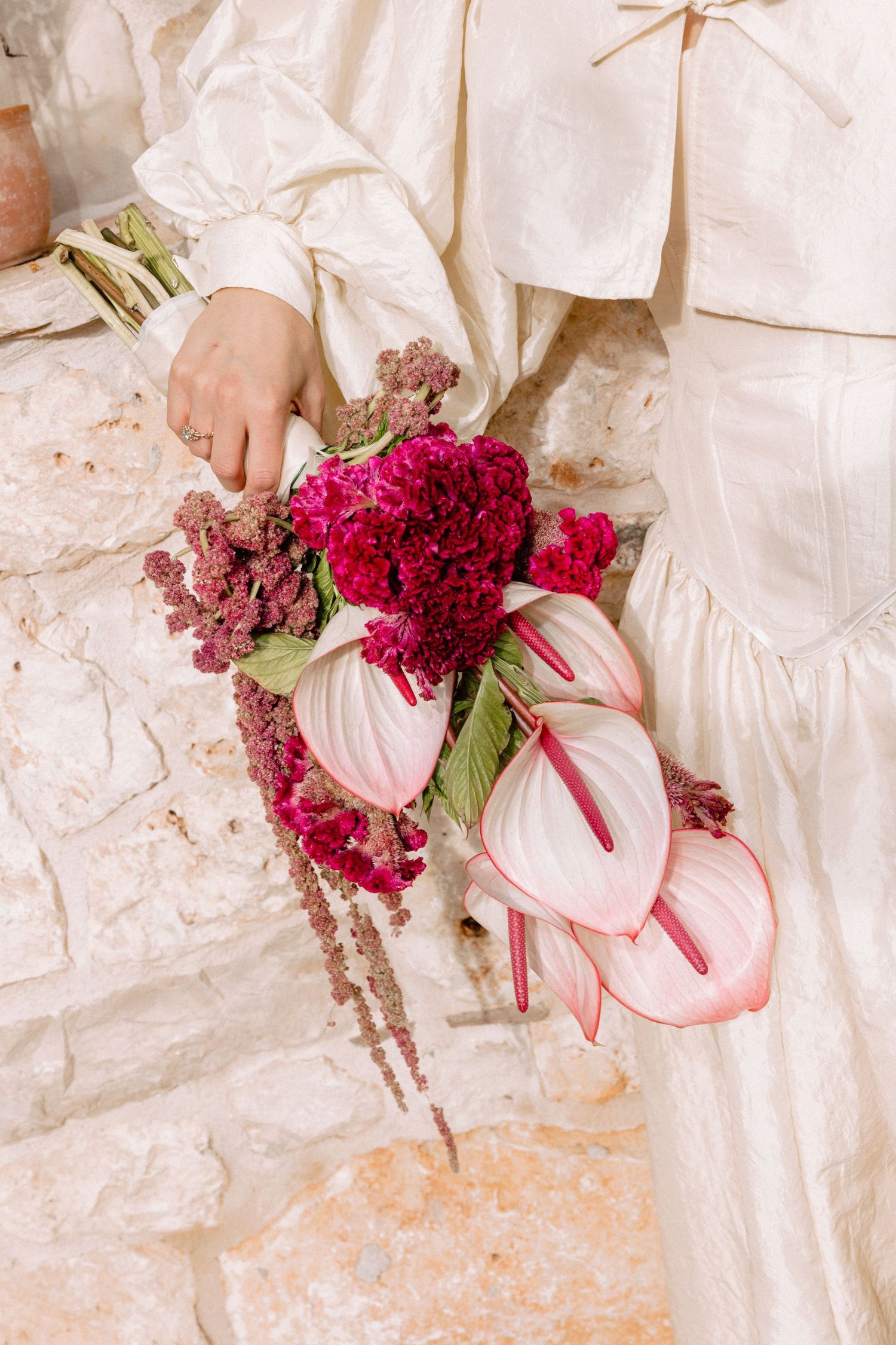Wedding bouquet featuring vibrant red flowers and anthurium against white fabric.