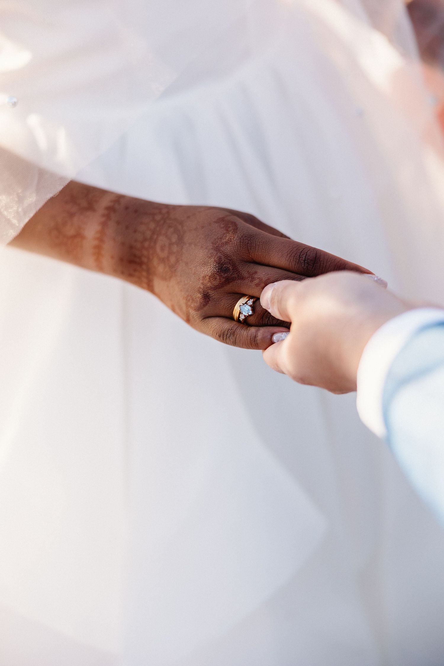 Close-up of interracial couple exchanging rings with henna-adorned hands.