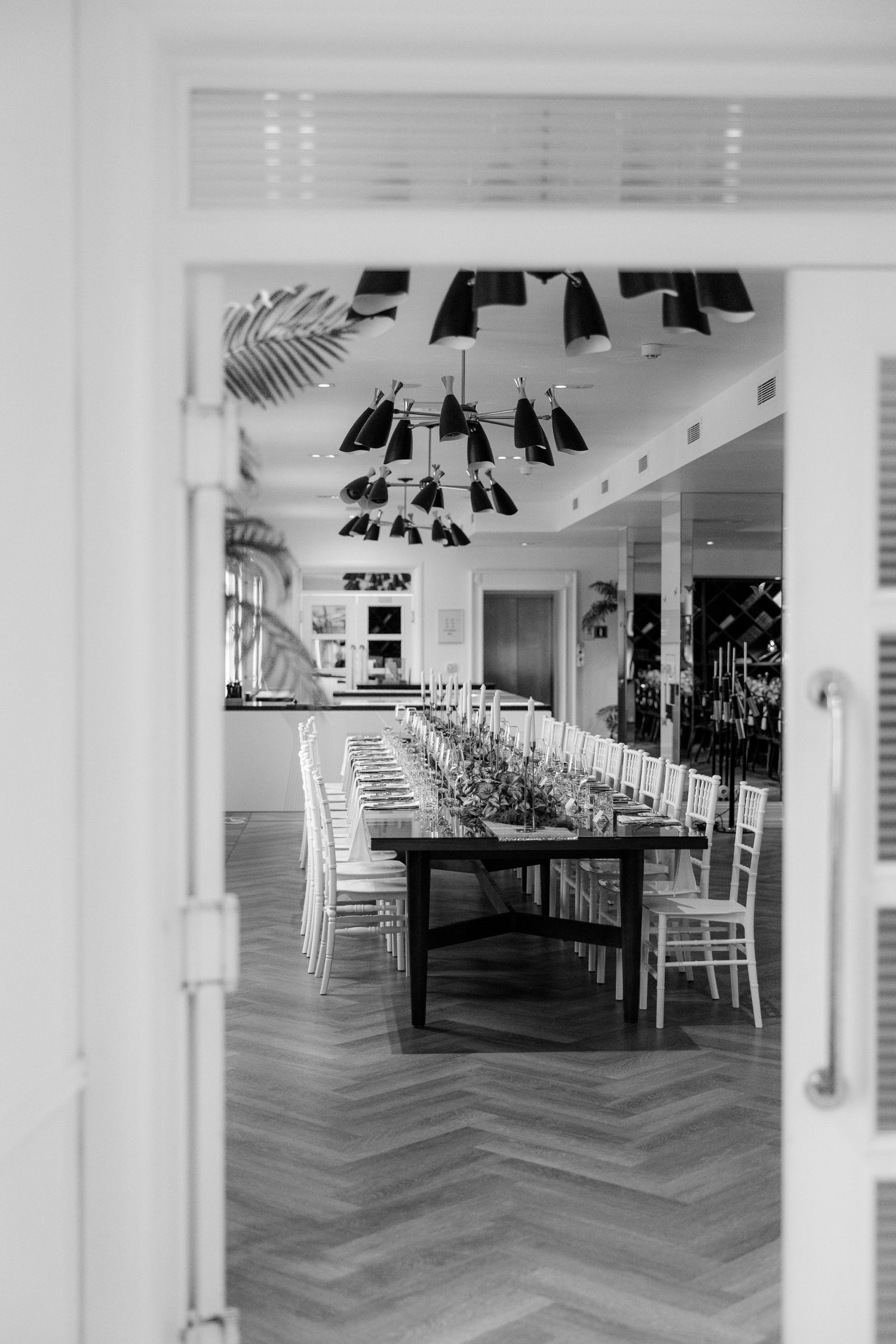 Elegant long dining table set for wedding reception viewed through open doorway in black and white.