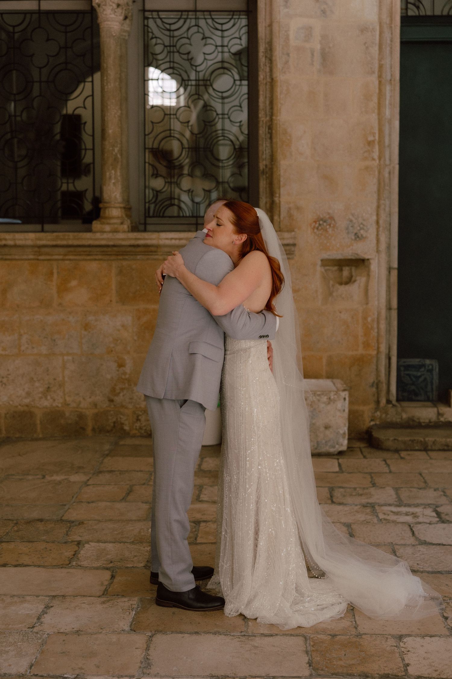 A romantic moment captured in a historic stone corridor with a lace wedding dress and grey suit  in Dubrovnik, Croatia.