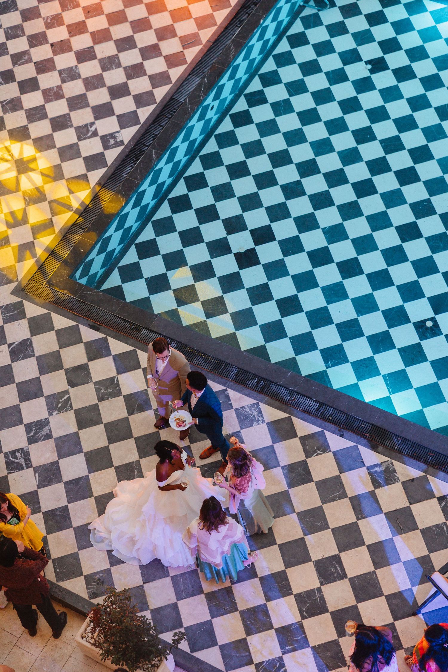 Aerial view of bride in white gown with wedding party on black and white checkered marble floor.