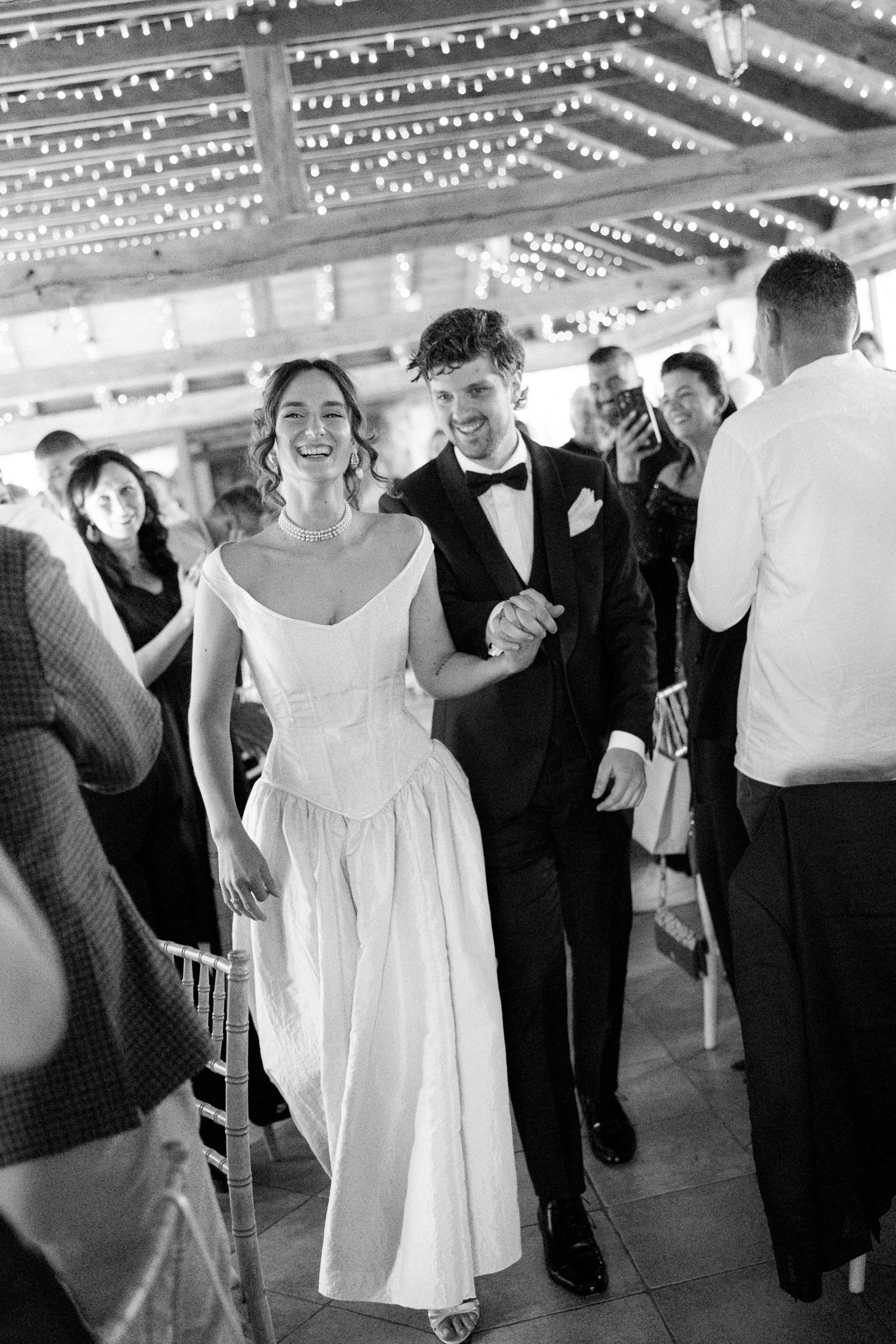 Wedding celebration under string lights with guests in formal attire dancing.