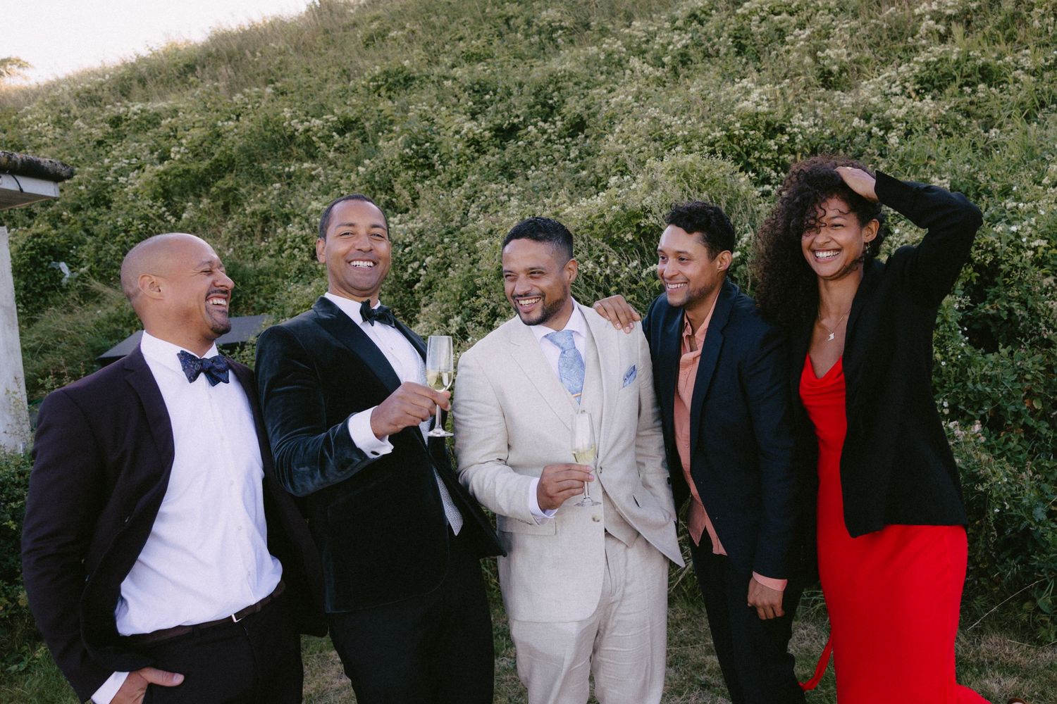 Wedding party members strike playful poses together outdoors during reception festivities.