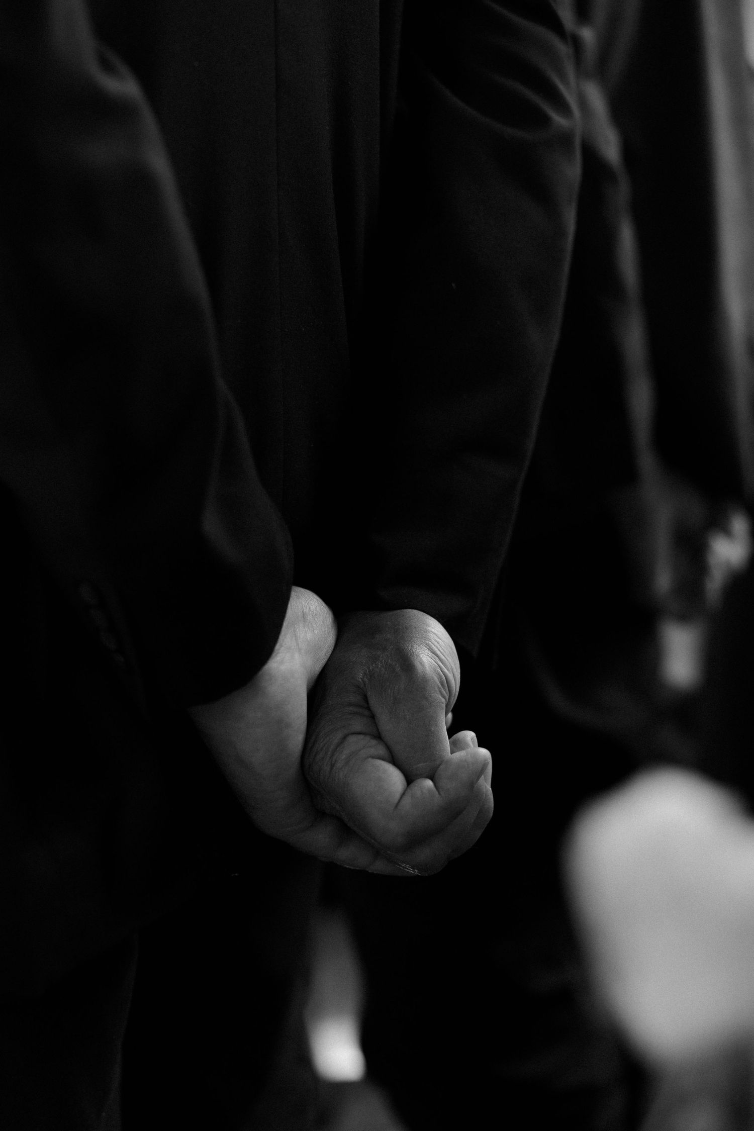 Black and white close-up of clasped hands during formal ceremony.