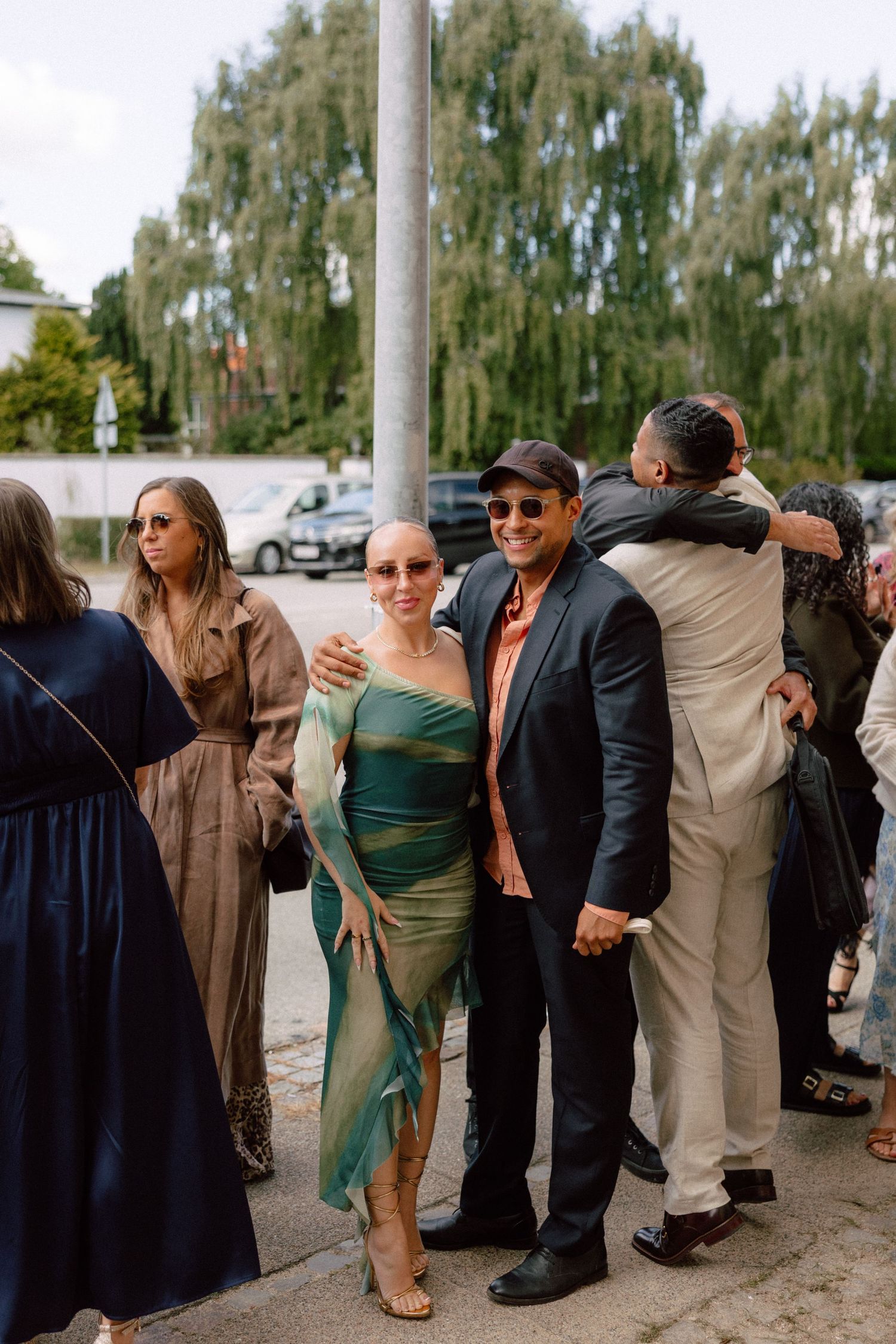 Wedding party members lined up against a wall outdoors in formal attire.