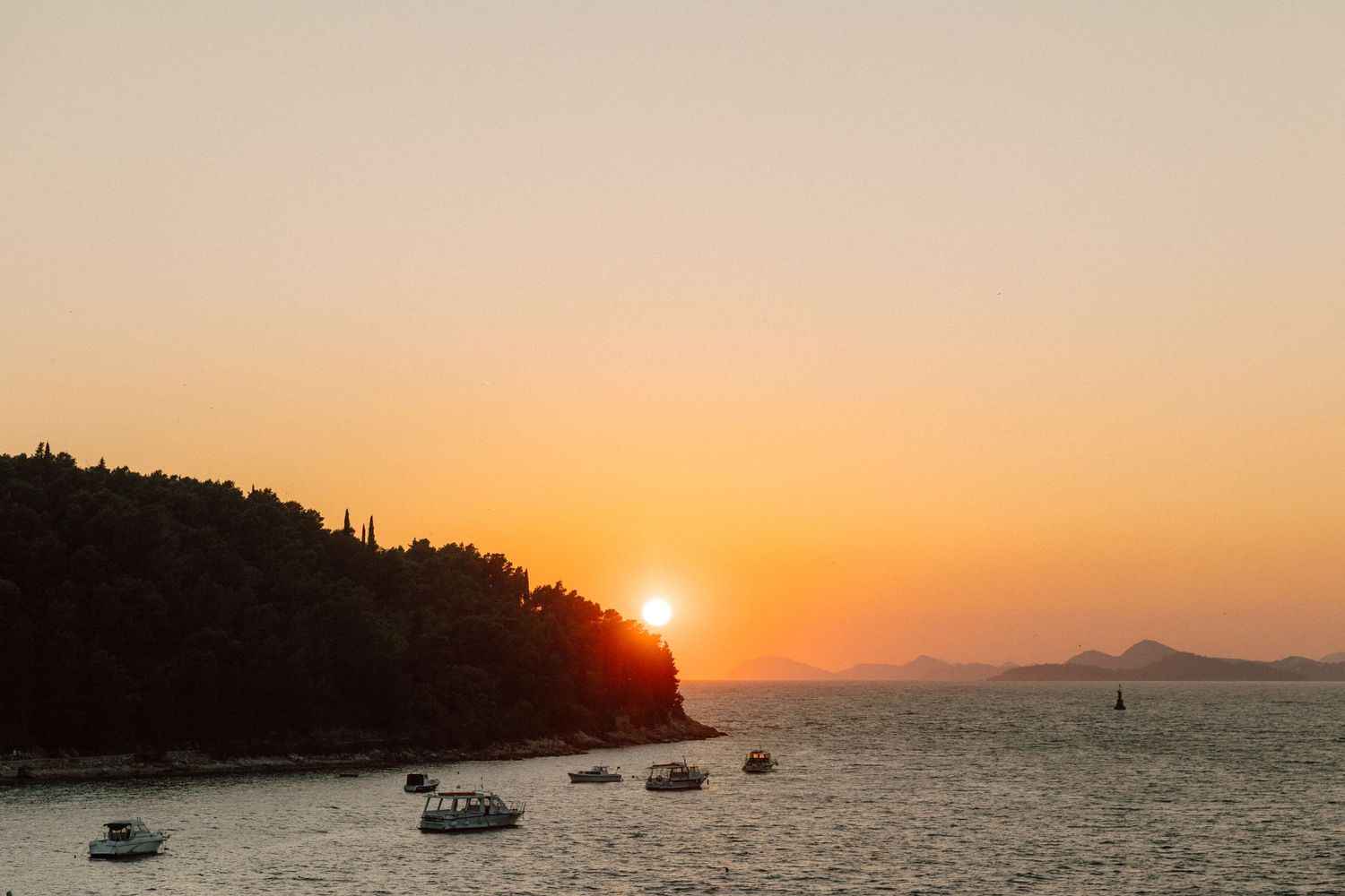 Beautiful sunset over the ocean with boats silhouetted against the orange sky.