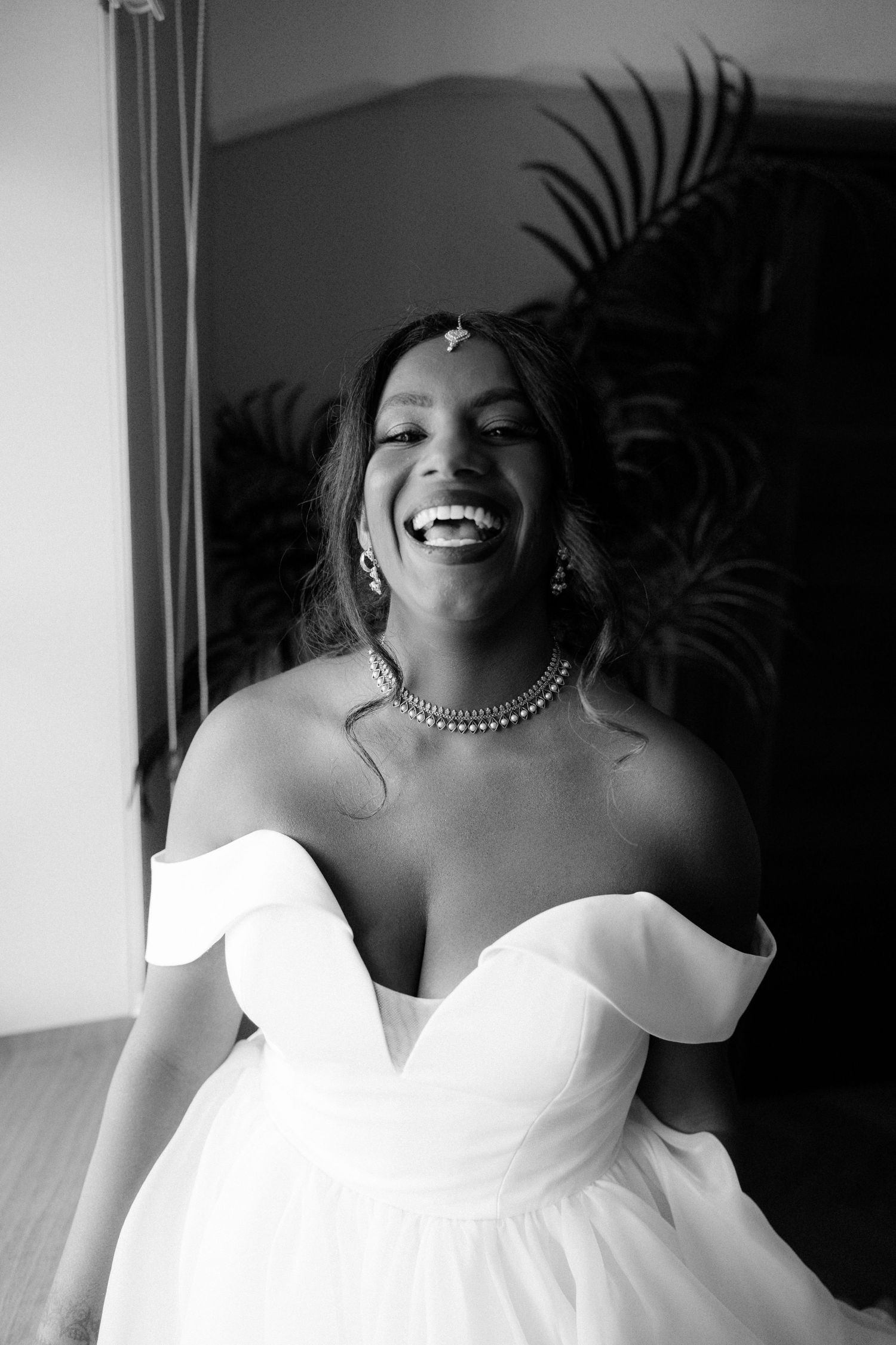 Joyful bride laughing in off-shoulder white ballgown wearing pearl necklace and bridal jewelry.