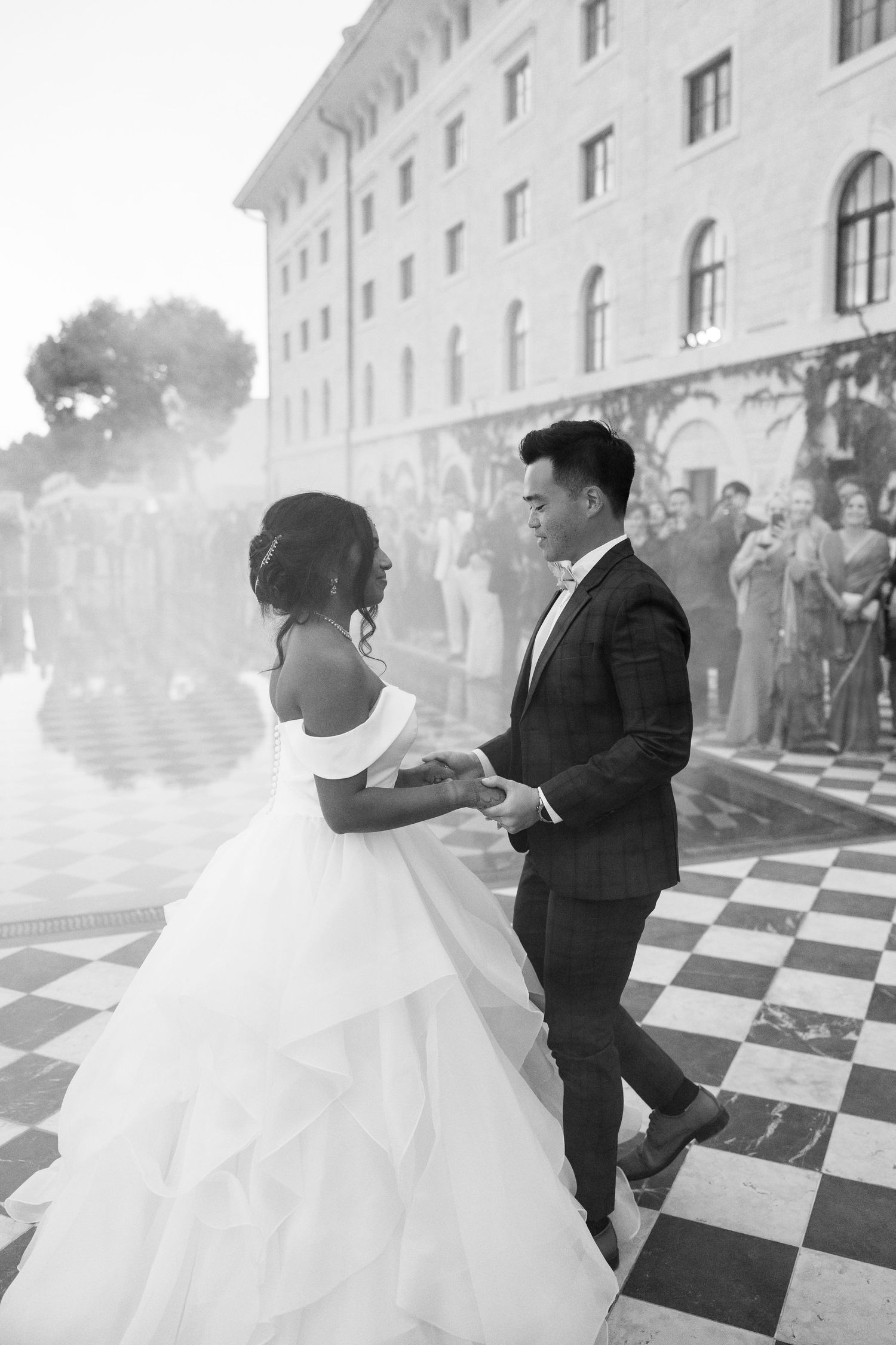 Black and white photo of bride and groom sharing first dance on checkered floor.