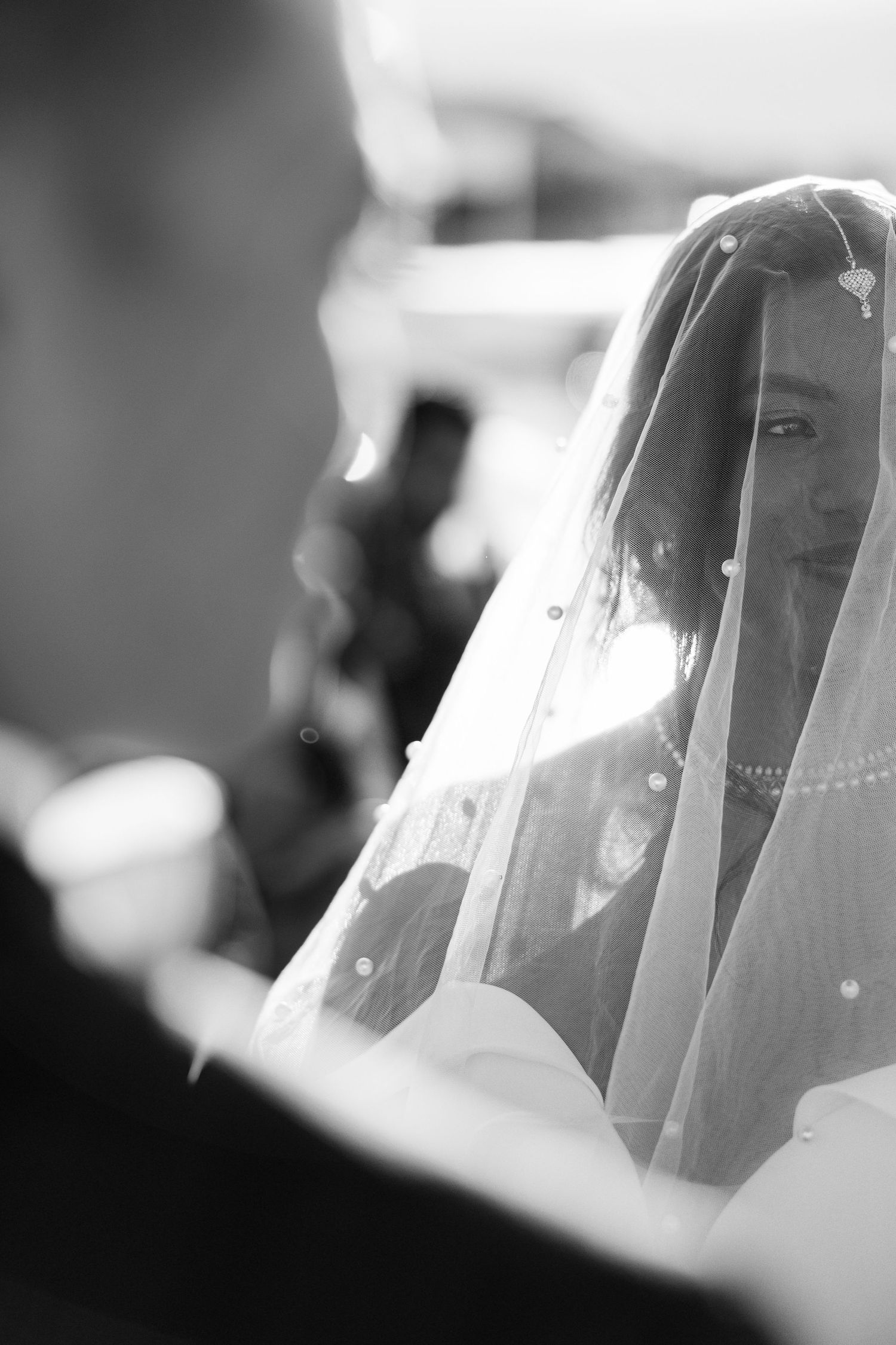 Black and white photo of a bride wearing a veil smiling at her groom during a wedding ceremony.