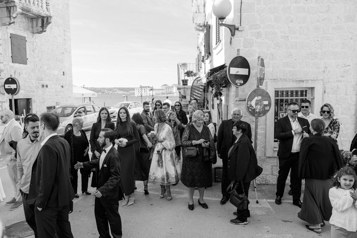 Black and white street scene of wedding guests gathering outside a building.