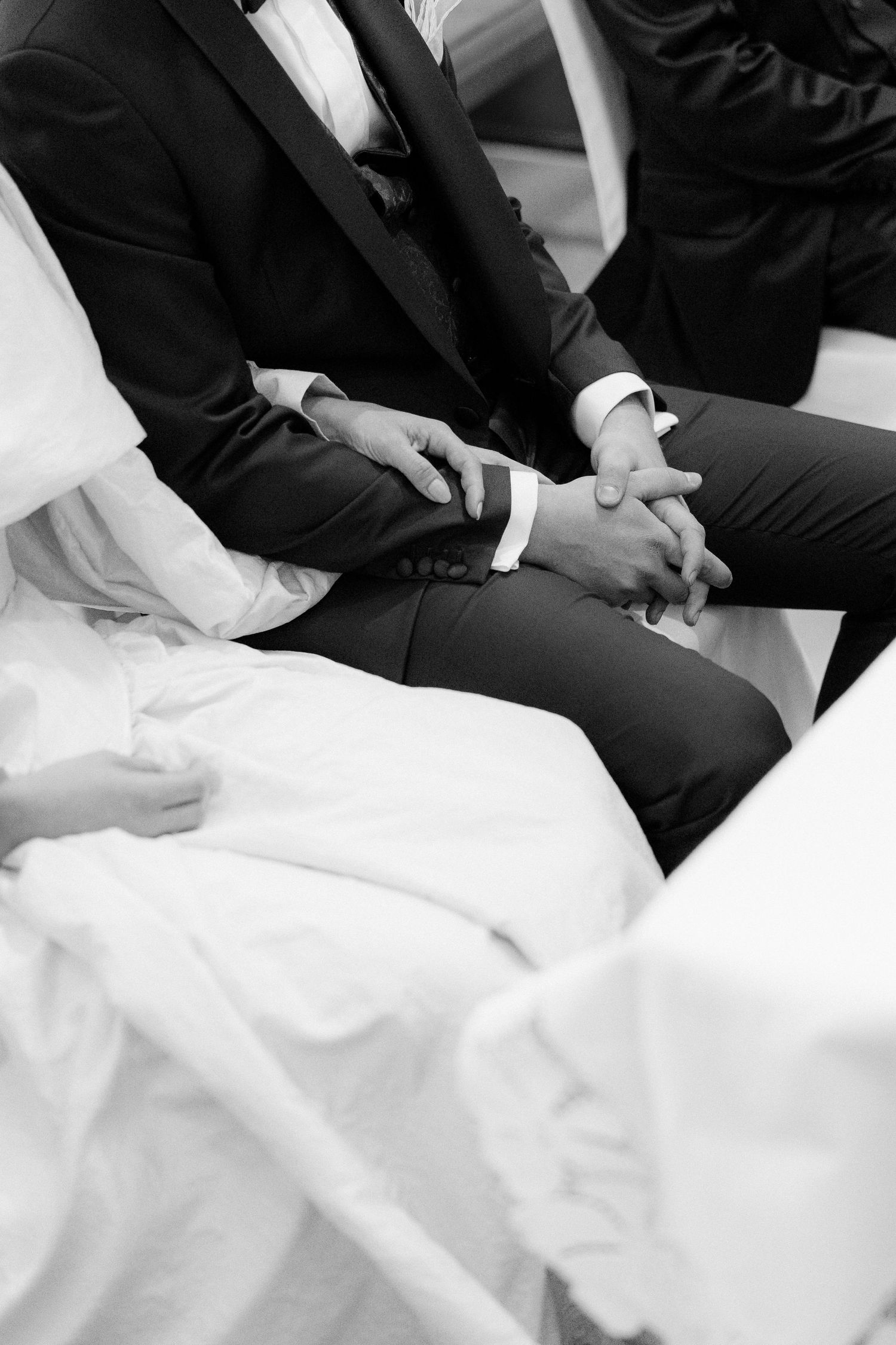 Close-up of bride and groom's hands during wedding ceremony in black and white.