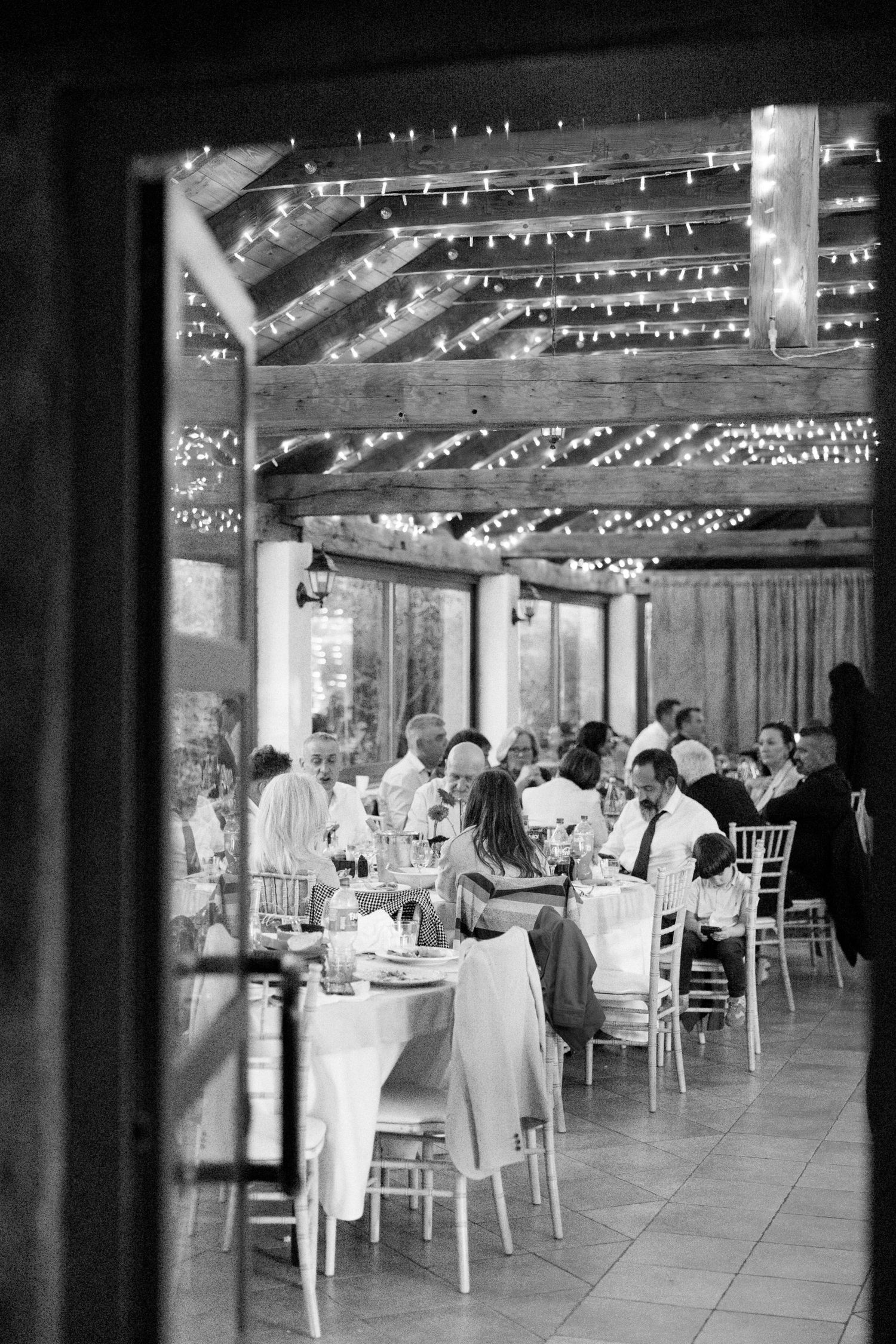 Reception venue interior with string lights and white table settings.