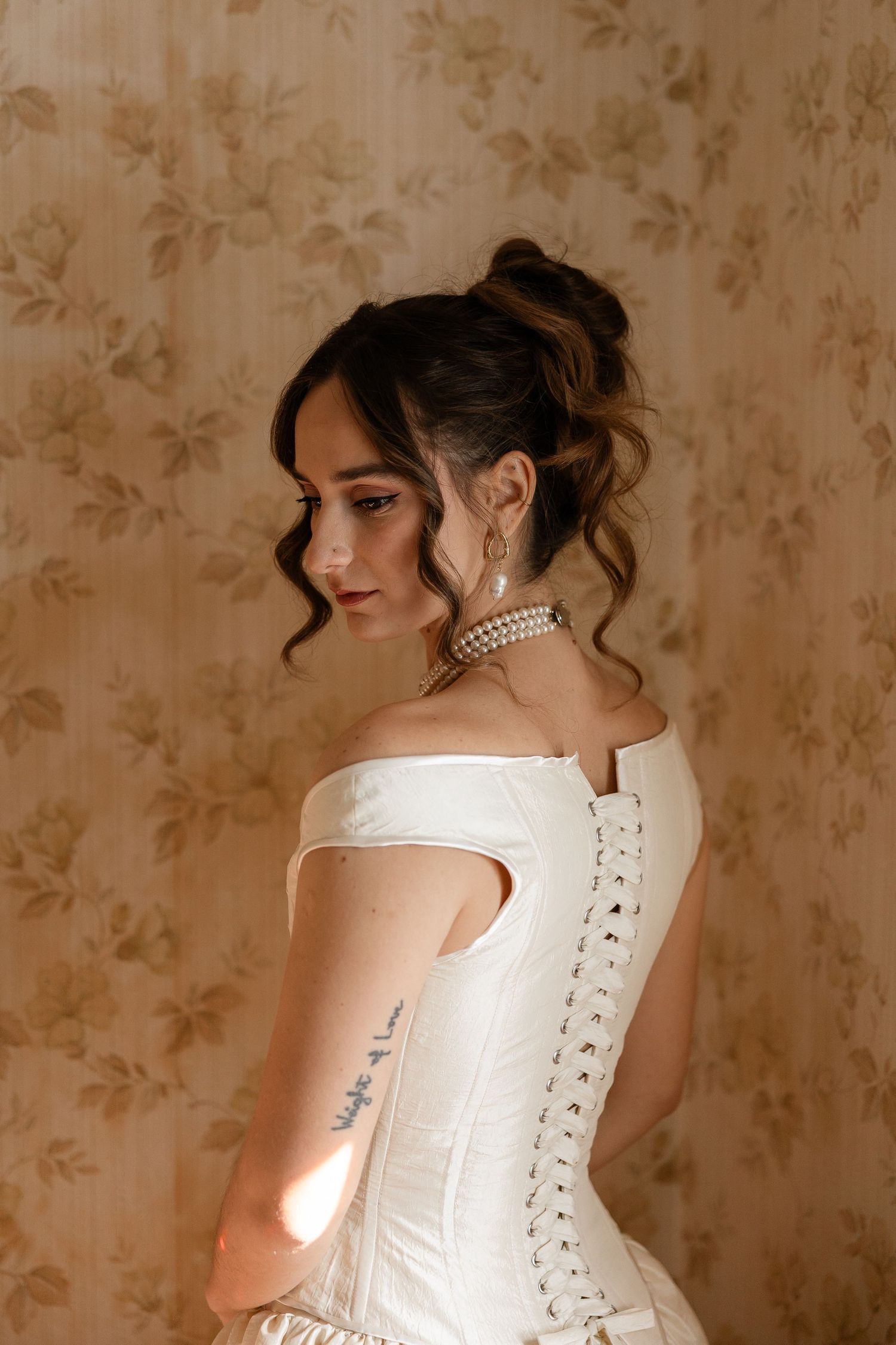 Back view of a corset-style white dress with lace-up detail against textured wallpaper.
