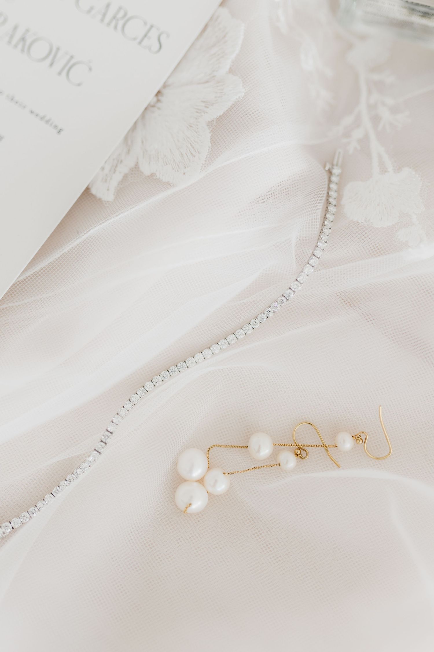 Delicate pearl earrings and crystal hairpiece laid on white lace fabric.