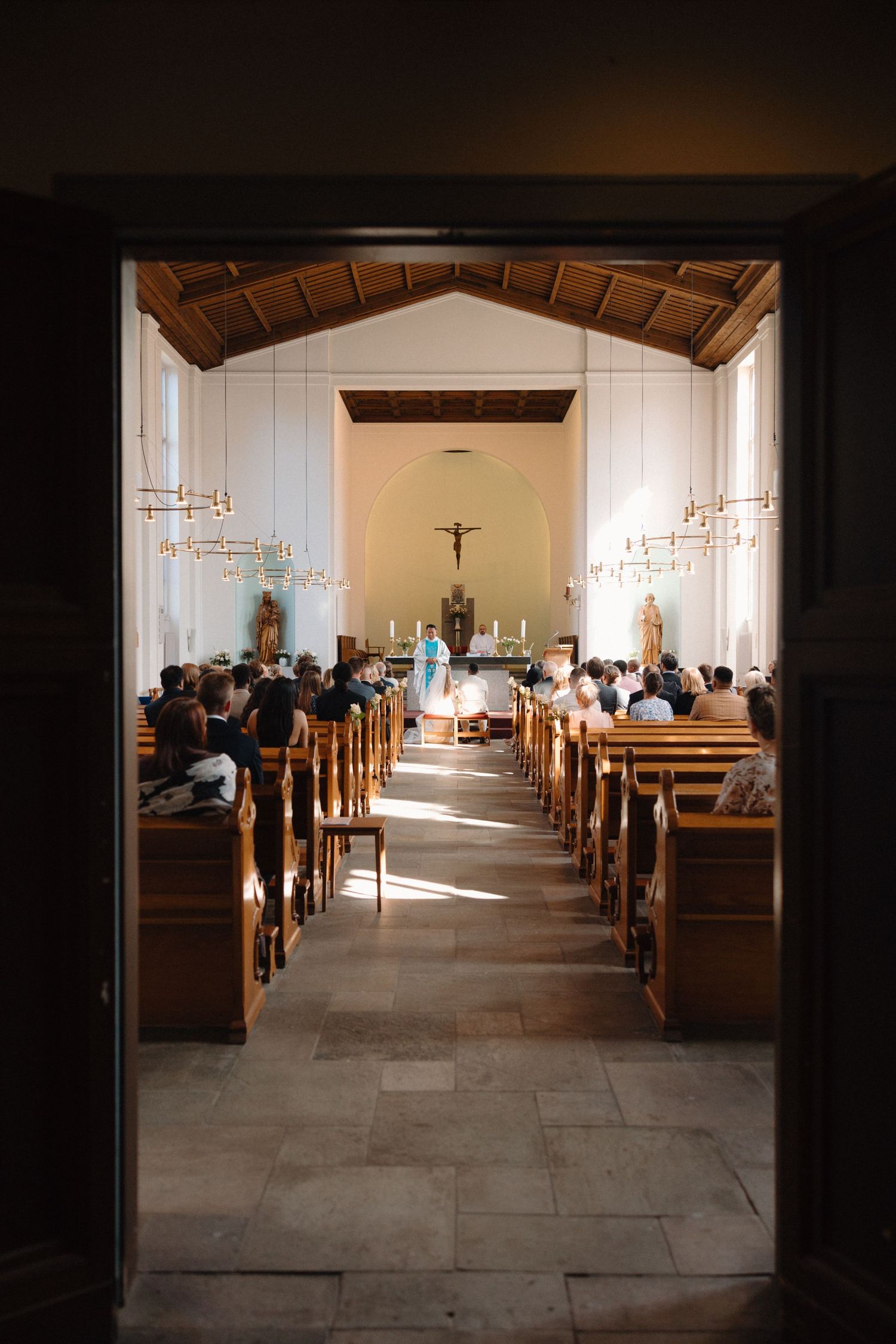 Sunlit church interior with wooden pews and crucifixes visible.