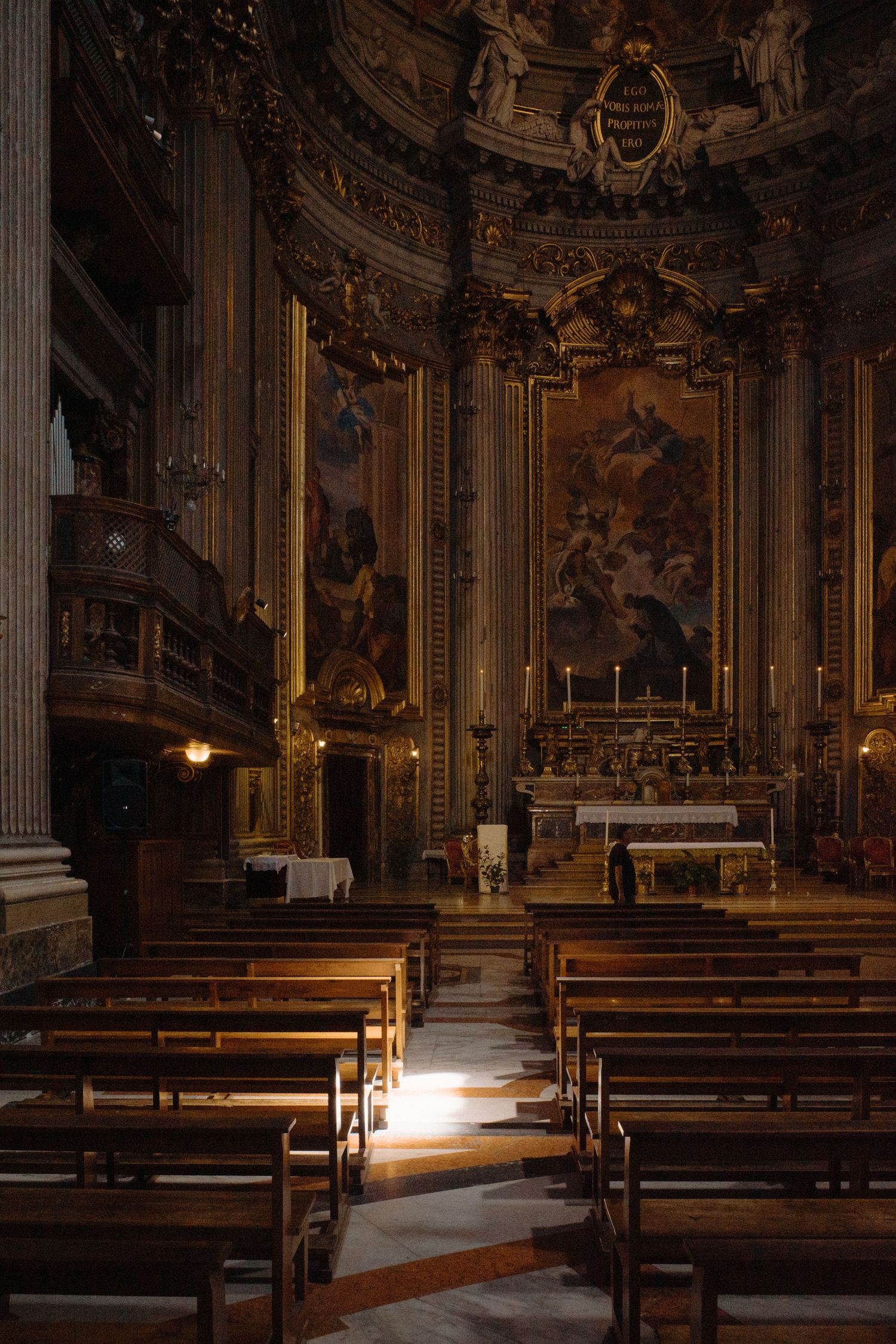 Ornate baroque church interior with wooden pews and dramatic lighting illuminating the altar and gilded decorative details.