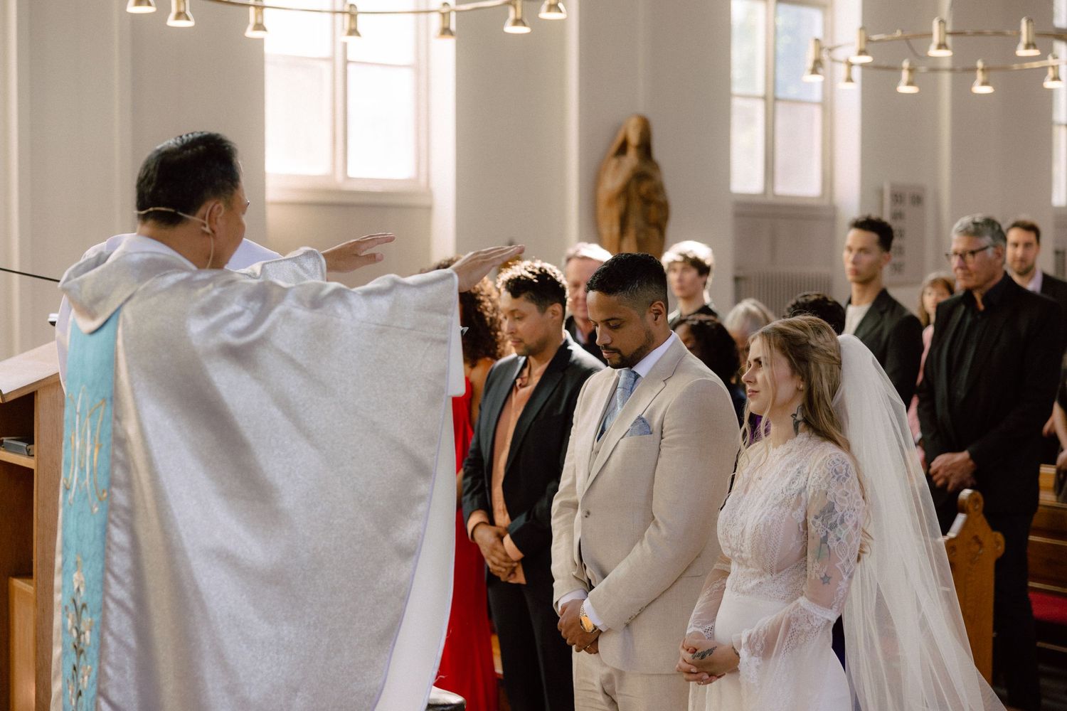 A joyous wedding ceremony takes place in a bright church interior with hanging lights and guests gathered.