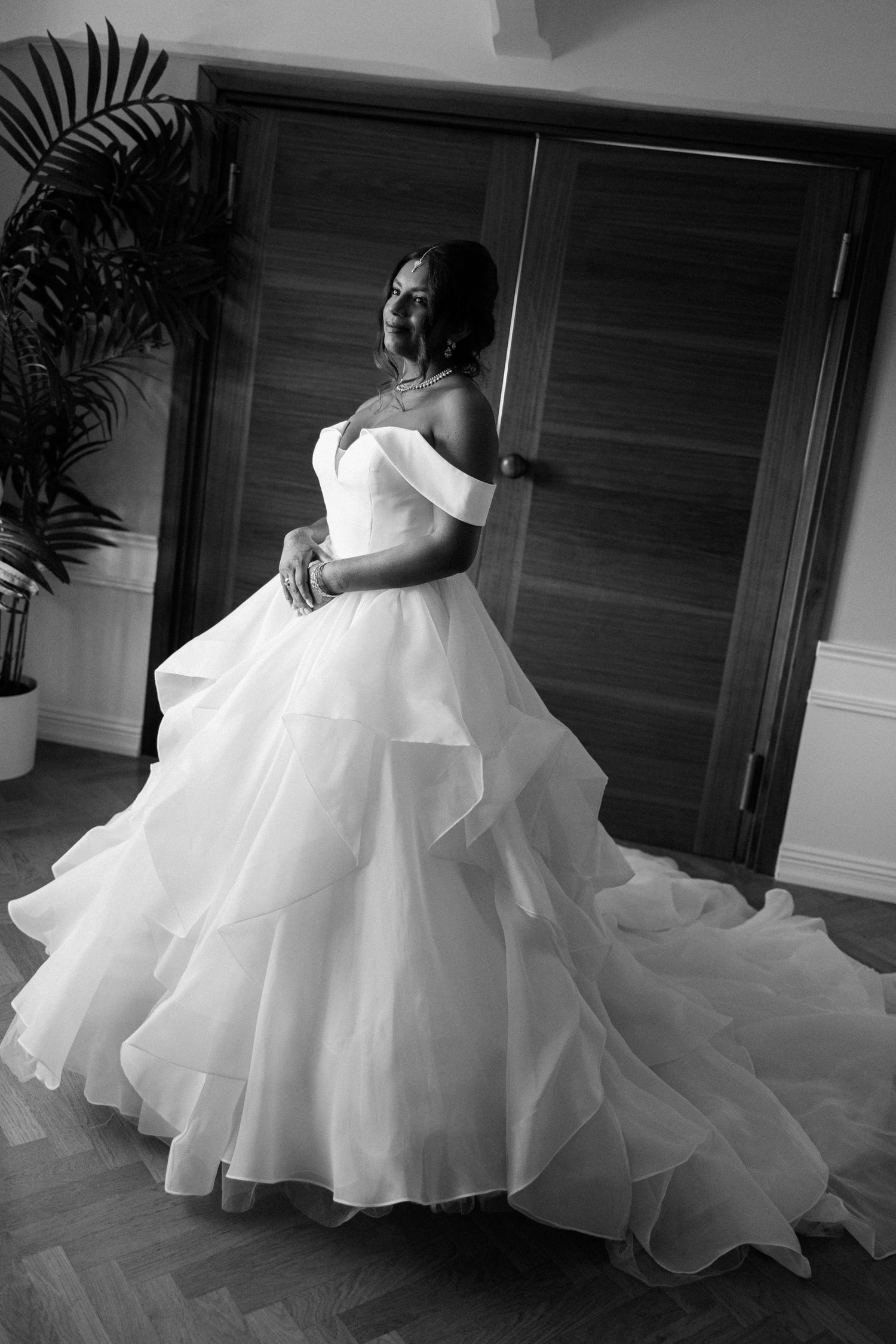 Black and white portrait of bride in stunning off-shoulder layered ball gown wedding dress.