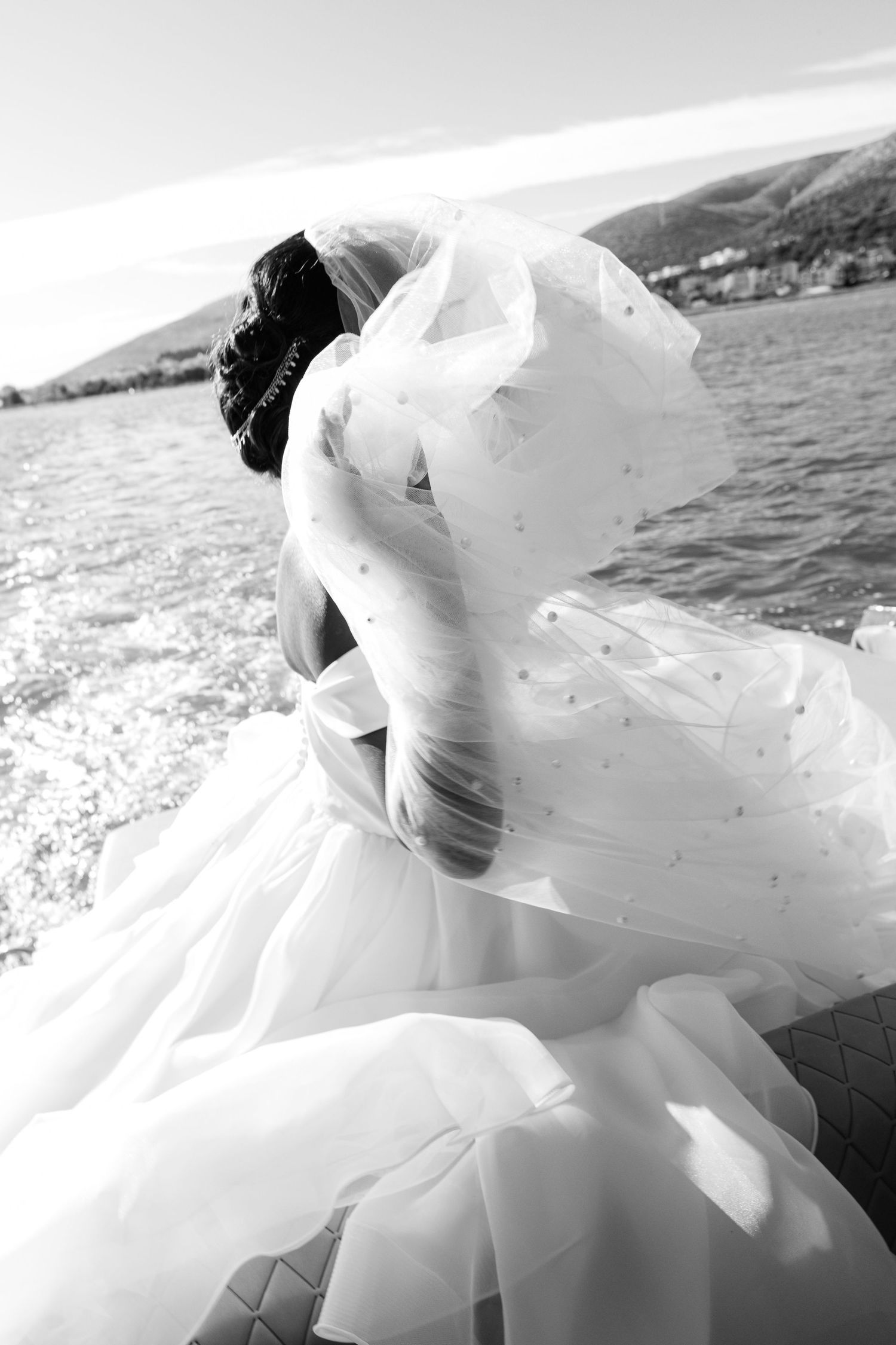 Black and white photo of a bride in a flowing wedding gown with veil blowing in the wind on a boat.