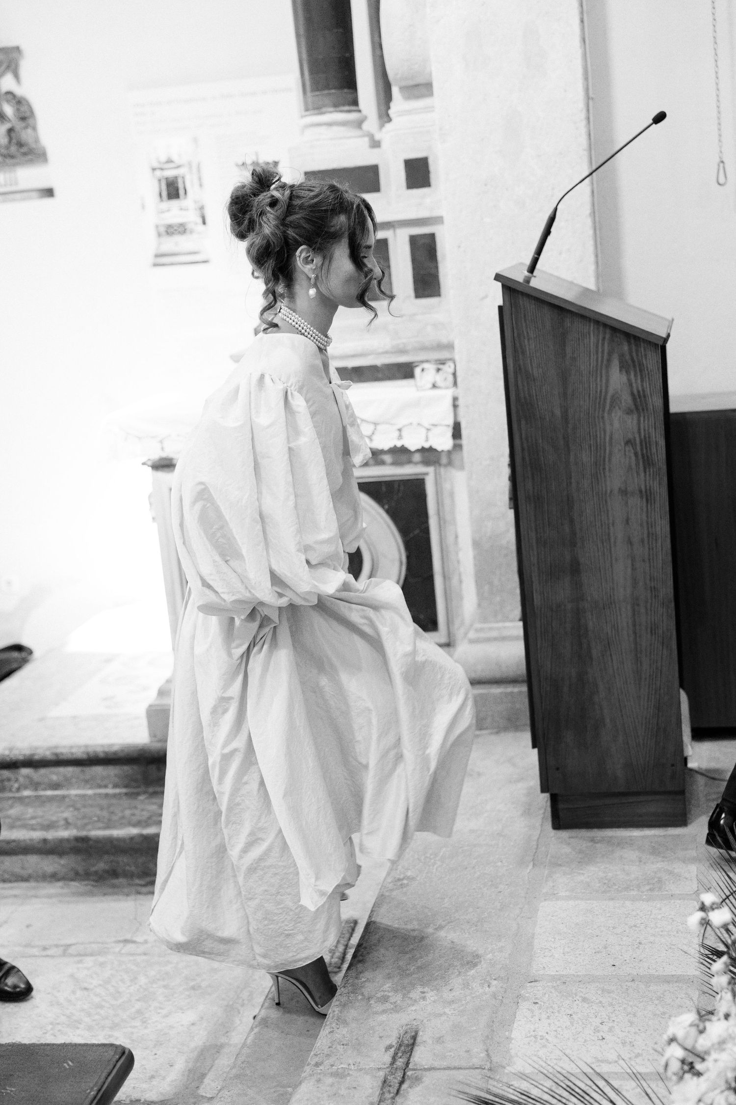 Black and white image of a person in white clothing walking through an interior space.