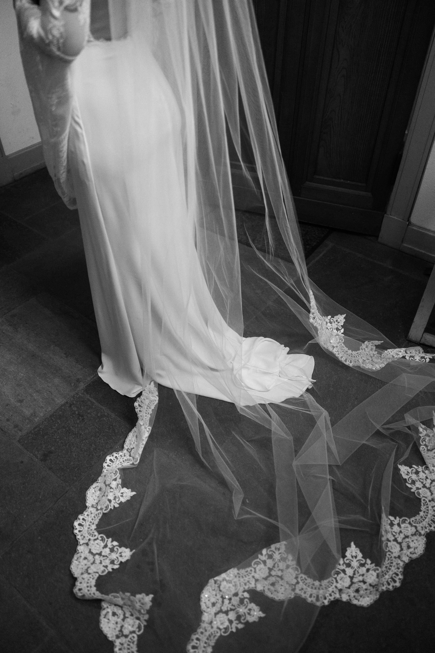 Close-up of a wedding dress train with delicate lace details on stone flooring.