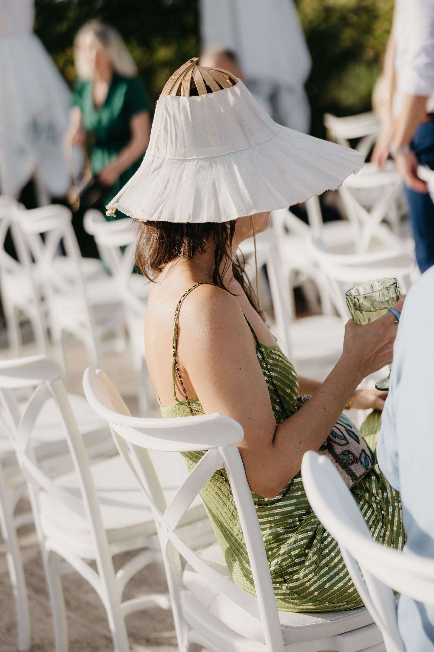 Guest in green dress and sun hat seated at outdoor white chairs in Italy.