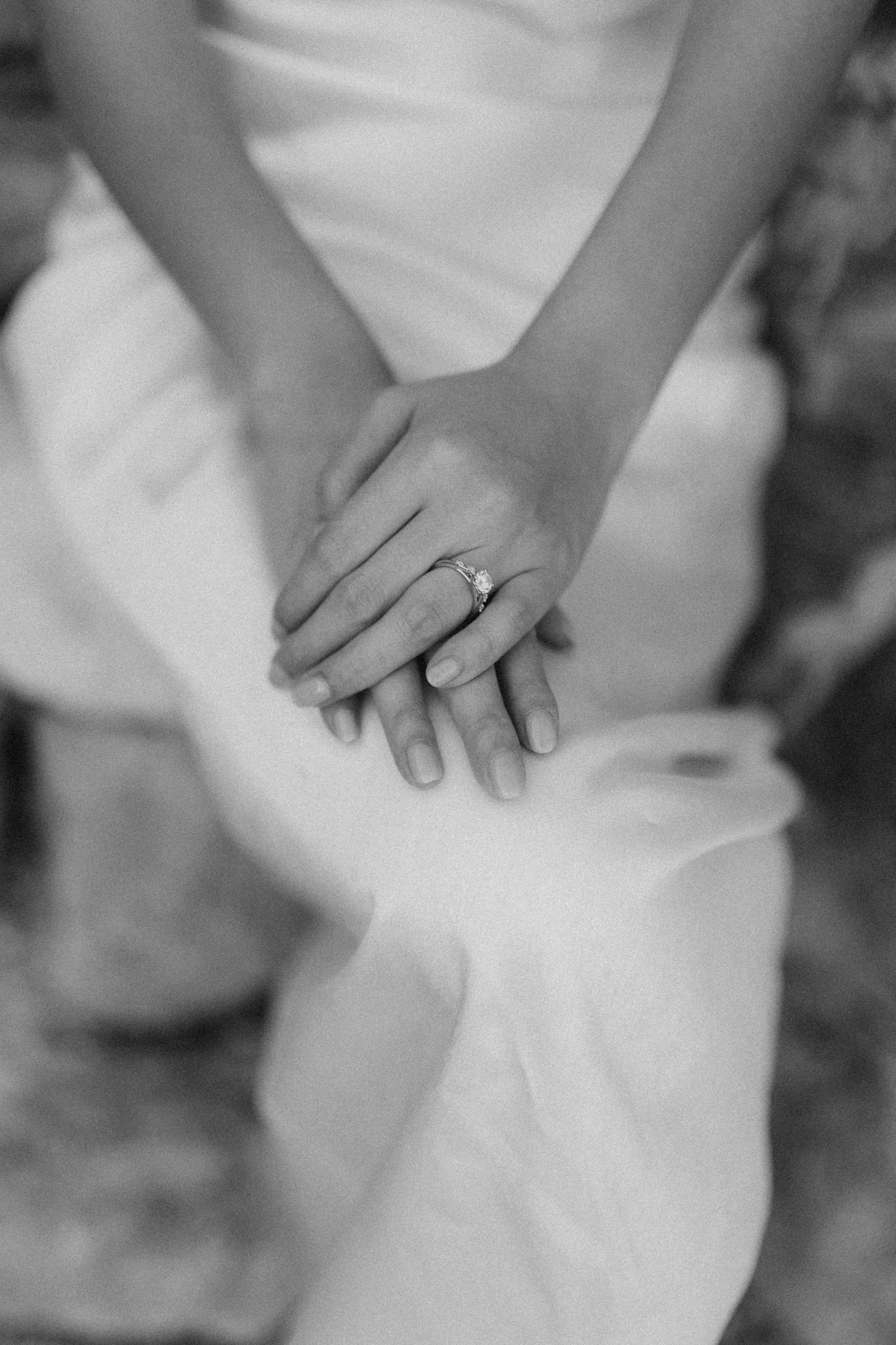 Black and white close-up of hands clasped together with engagement ring showcasing an intimate wedding moment.