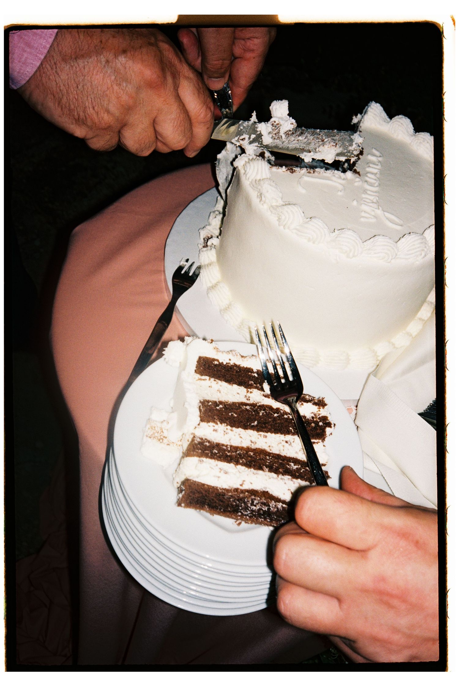 Hands cutting a white frosted layered wedding cake with chocolate layers visible on a white plate.