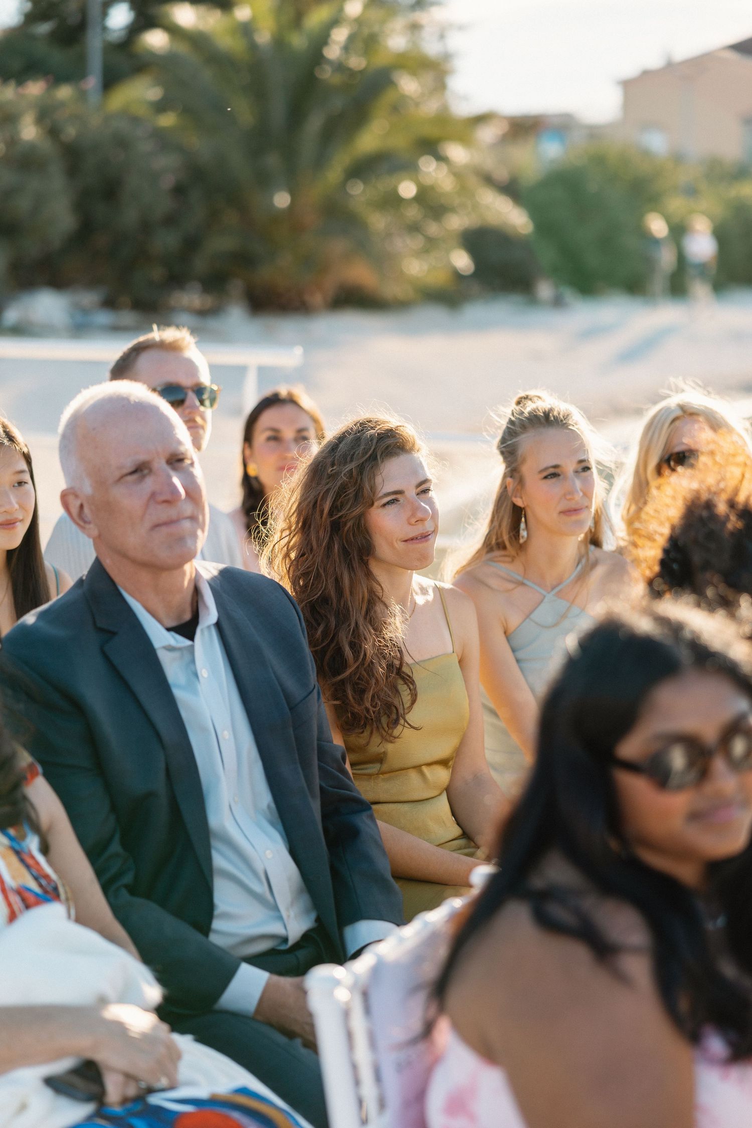 Wedding guests seated outdoors in golden sunlight watching ceremony attentively.
