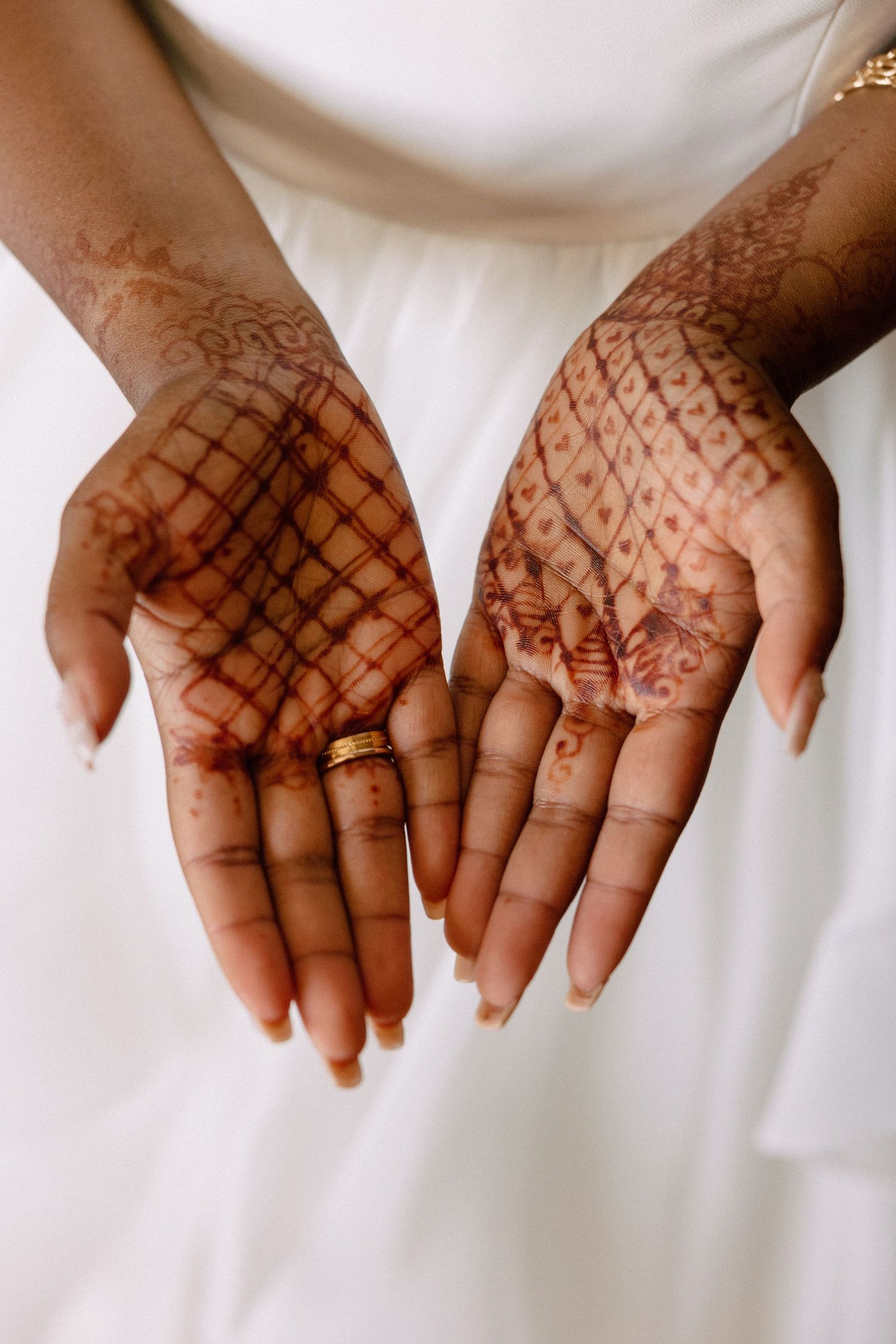 Close-up of bride's hands adorned with intricate henna mehndi designs and gold wedding ring.