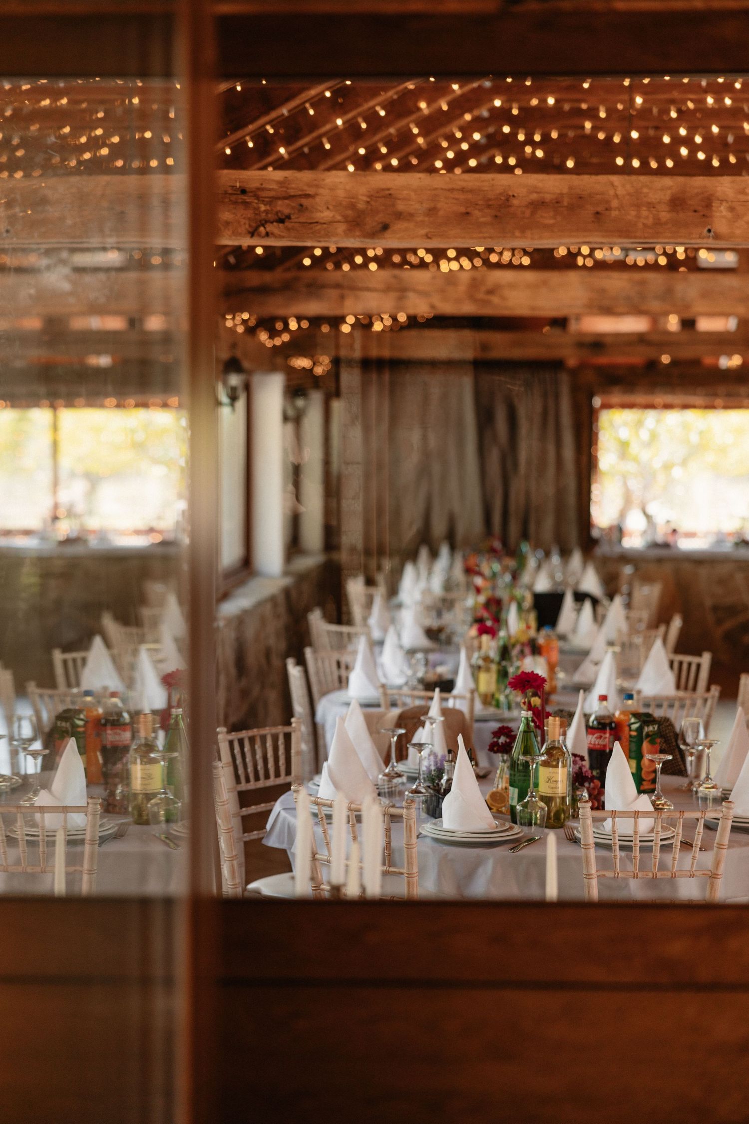 Wedding reception venue with rustic wooden beams and twinkling lights illuminating elegant table settings.